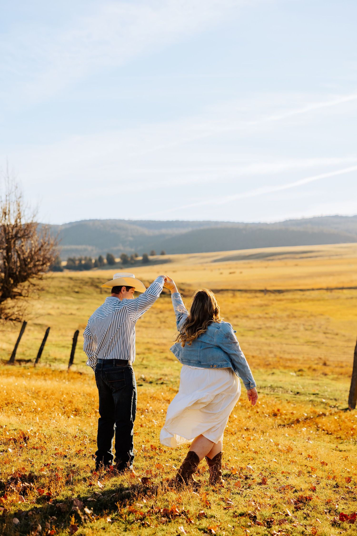 A couple poses playfully in a sunlit meadow with mountains visible in the distance.
