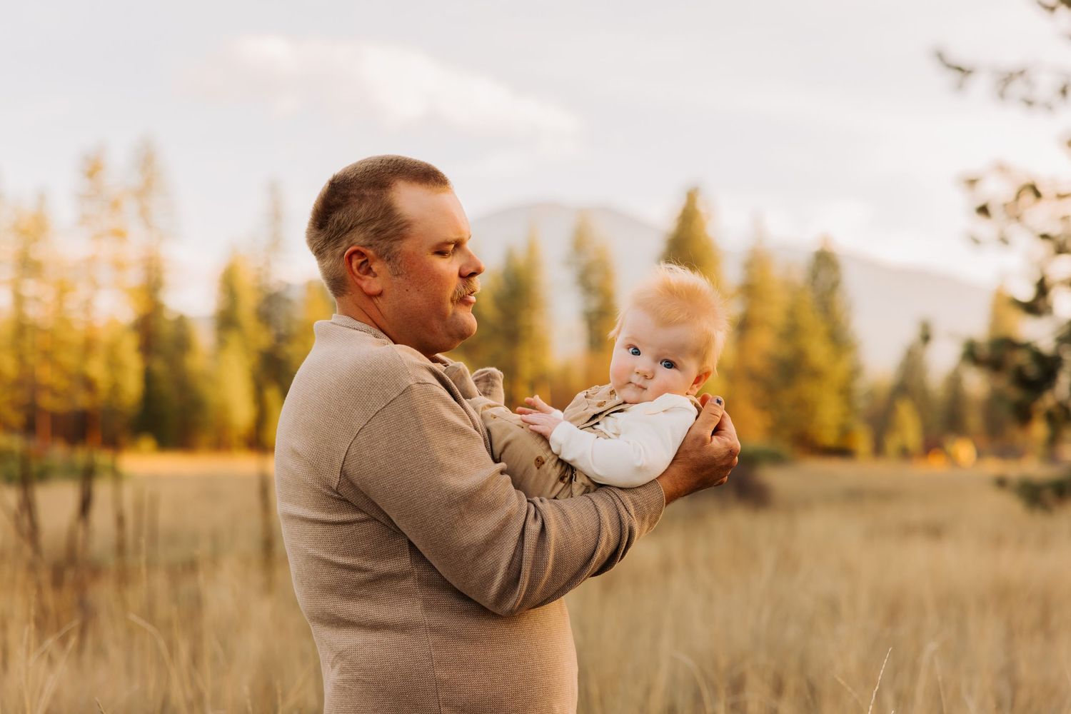 A tender moment between father and baby in a scenic mountain field.
