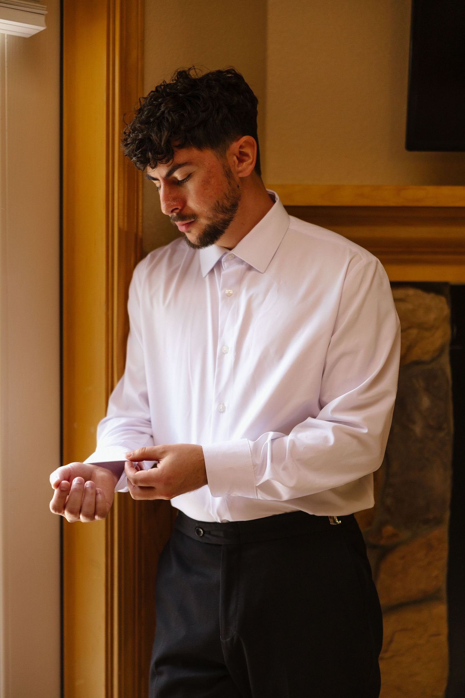 Handsome groom in white dress shirt fastening cufflinks while getting ready for his wedding day.