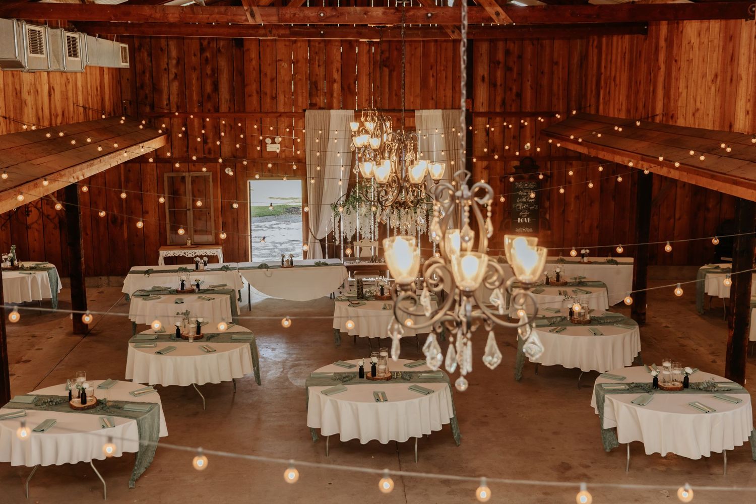 Elegant barn reception venue with crystal chandeliers and round tables set for a wedding.