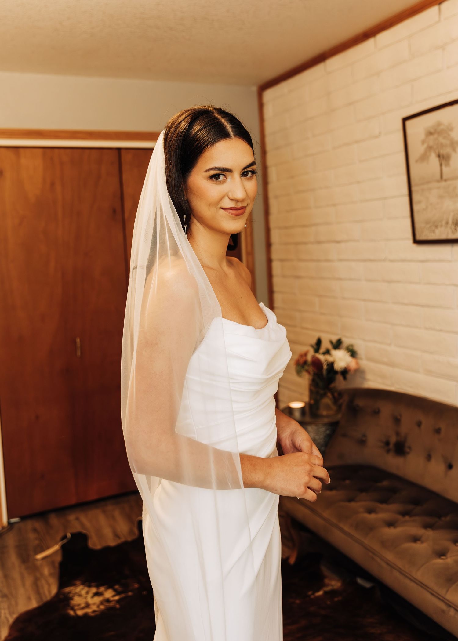Bride in elegant white dress posing against white brick wall in preparation room.