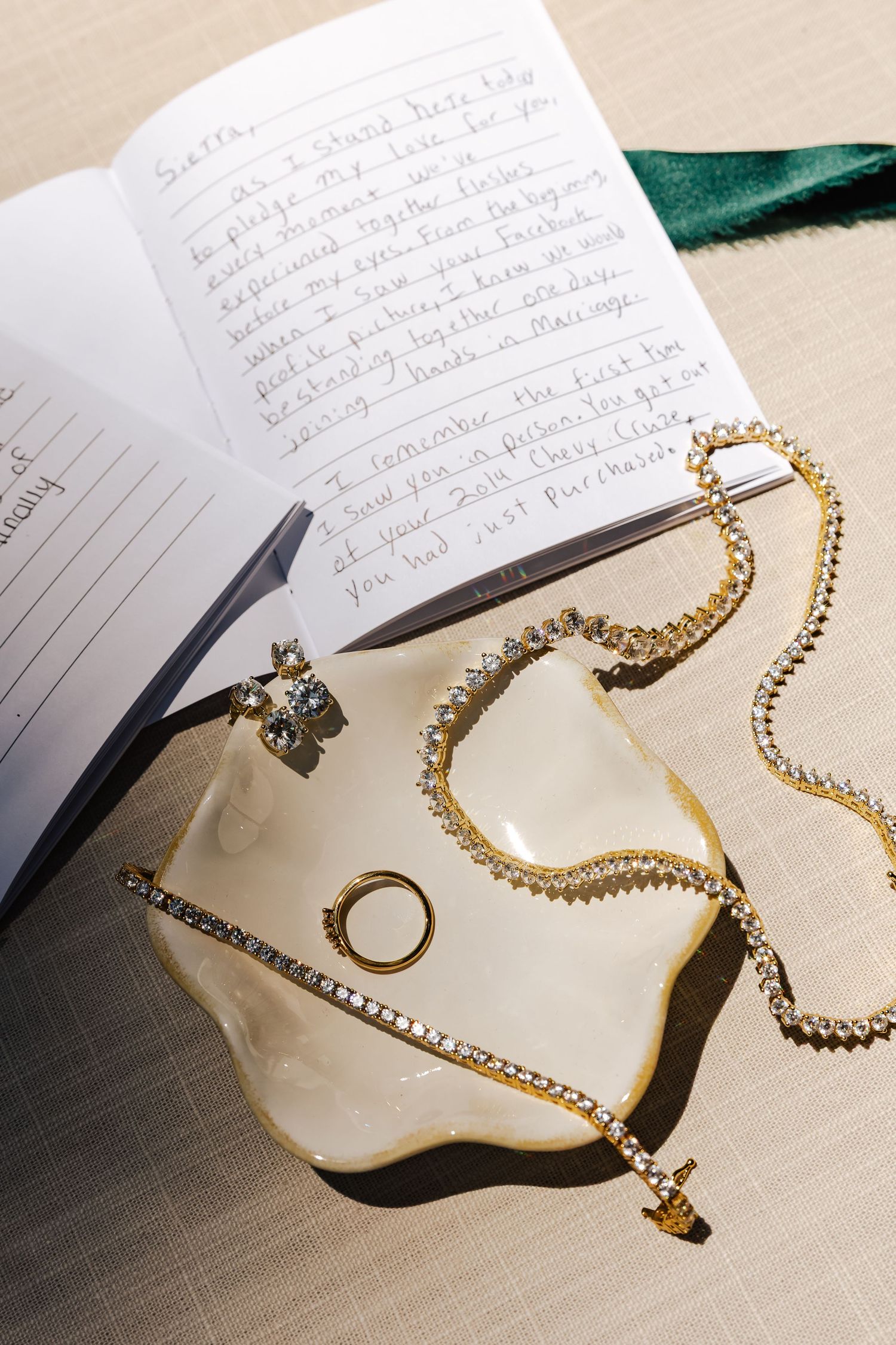 Gold diamond tennis necklace and ring in a white dish beside an open journal with handwritten notes.