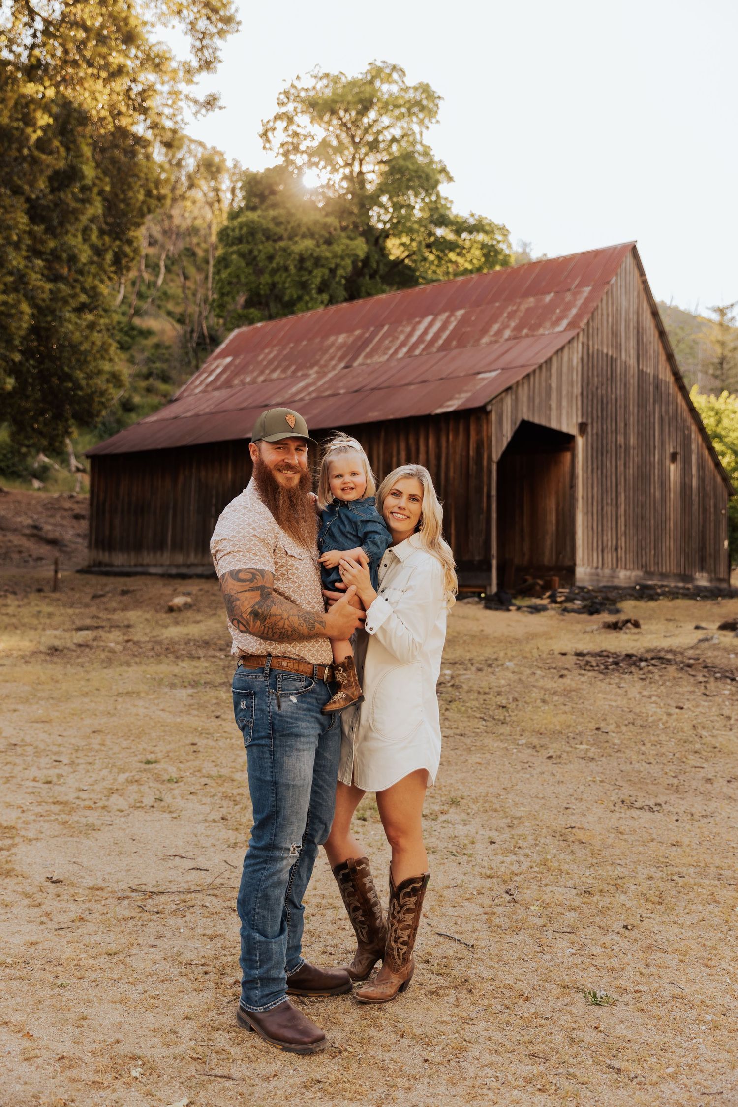 People gather near an old barn in a rustic countryside setting during golden hour.