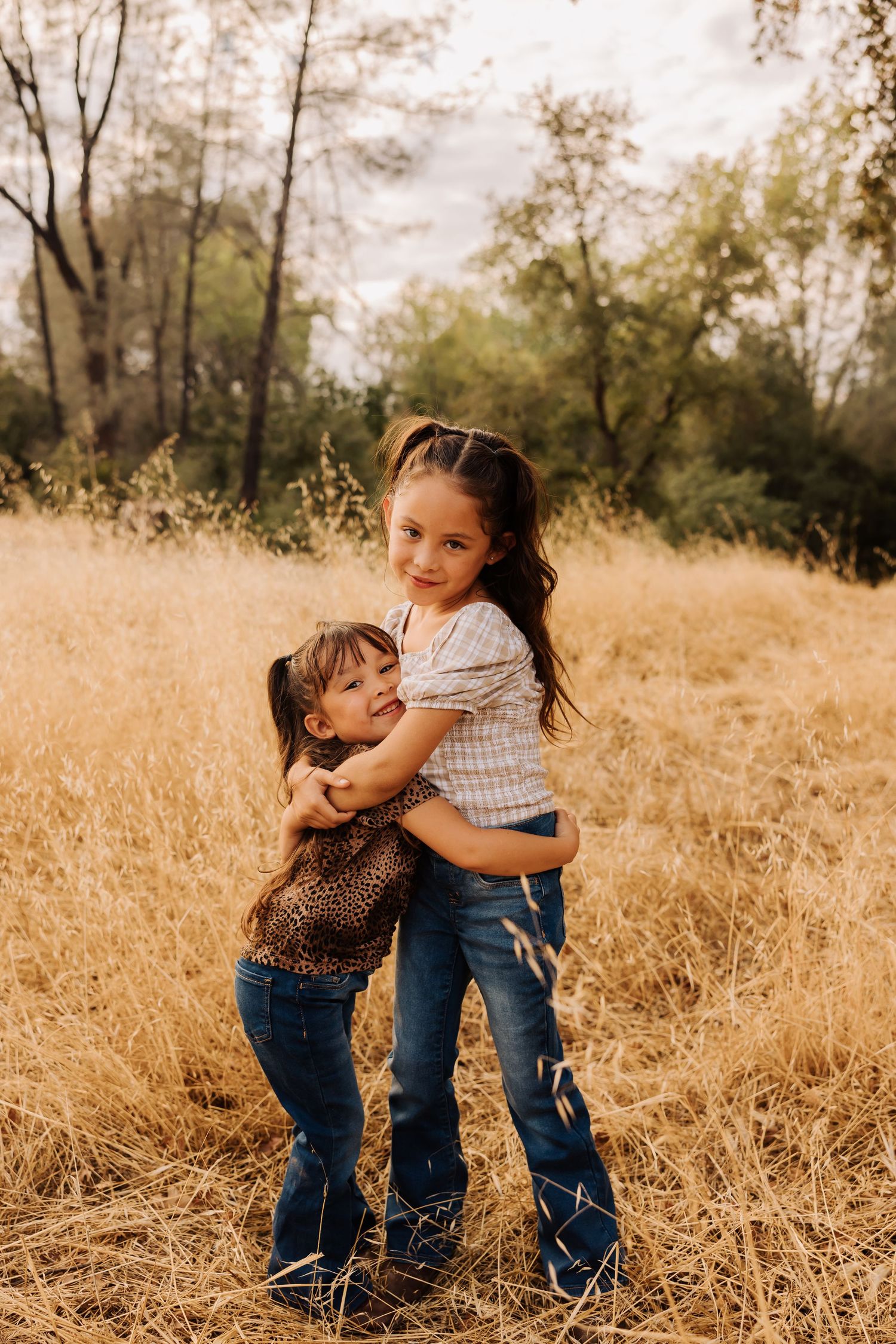 Siblings embrace while playing in tall golden grass during sunset.