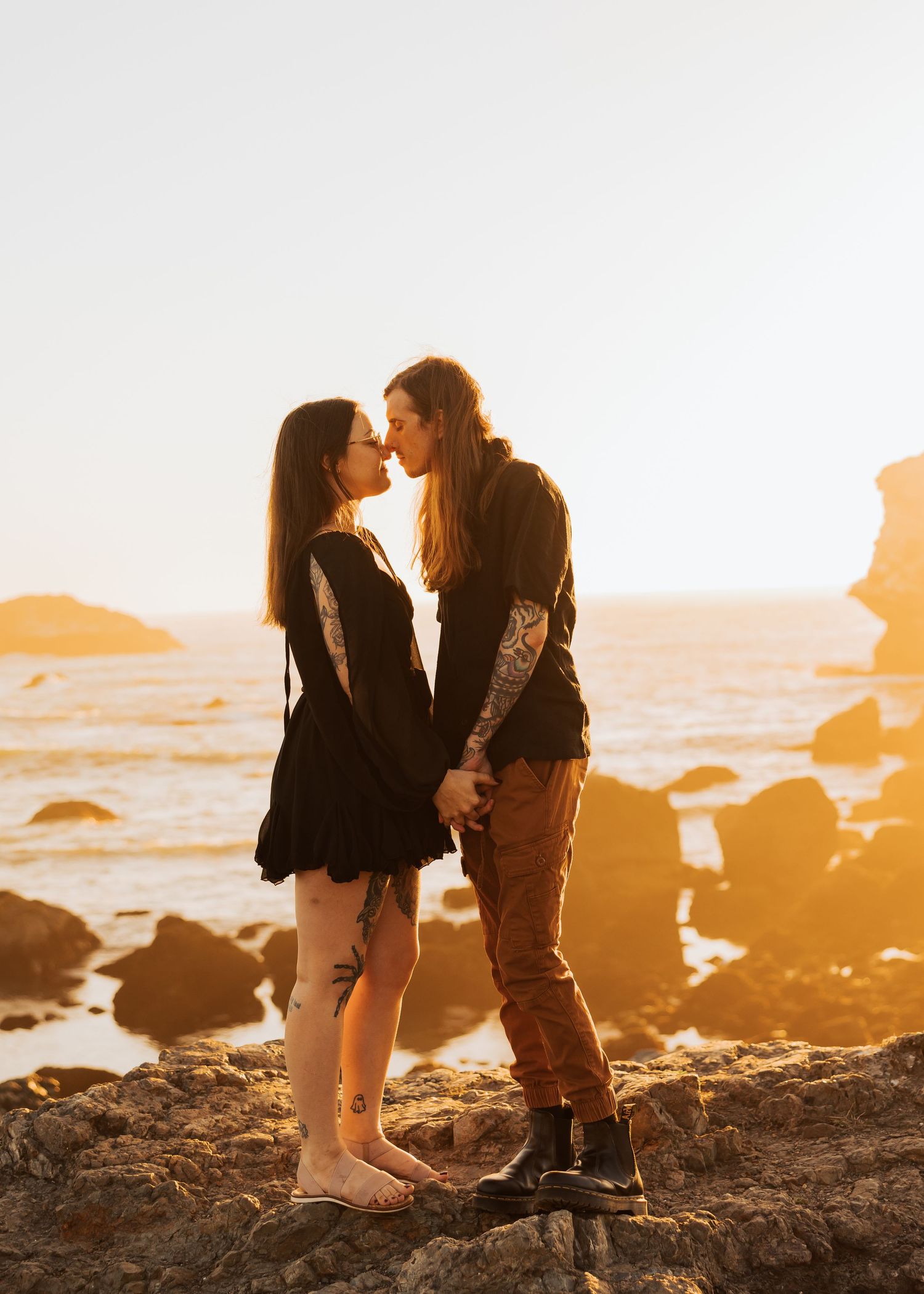 A romantic moment captured between two people on rocky coast at sunset.