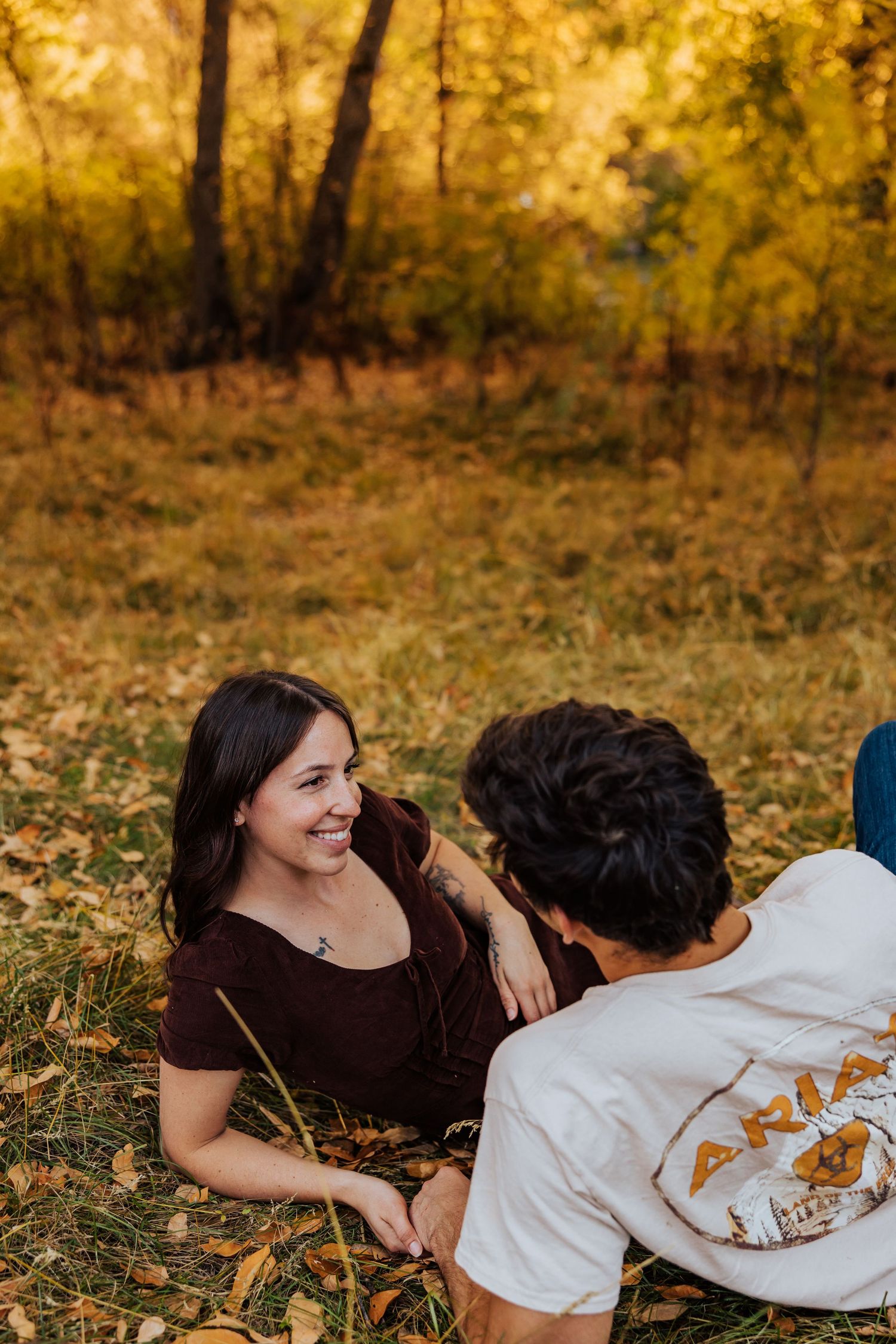 Couple having a tender moment while lying on autumn ground surrounded by golden foliage.