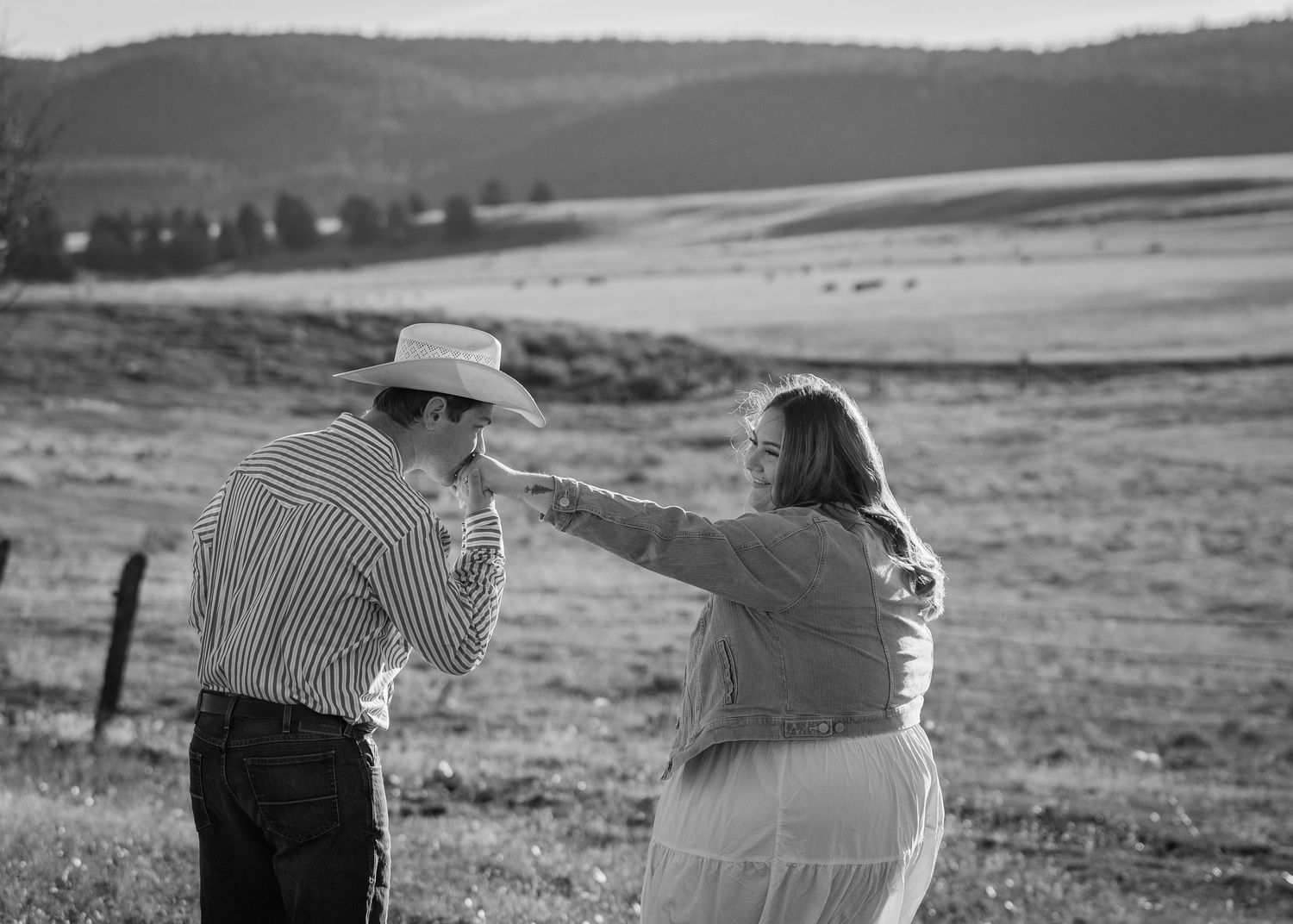 A couple sharing tender moments against a scenic rural landscape backdrop.