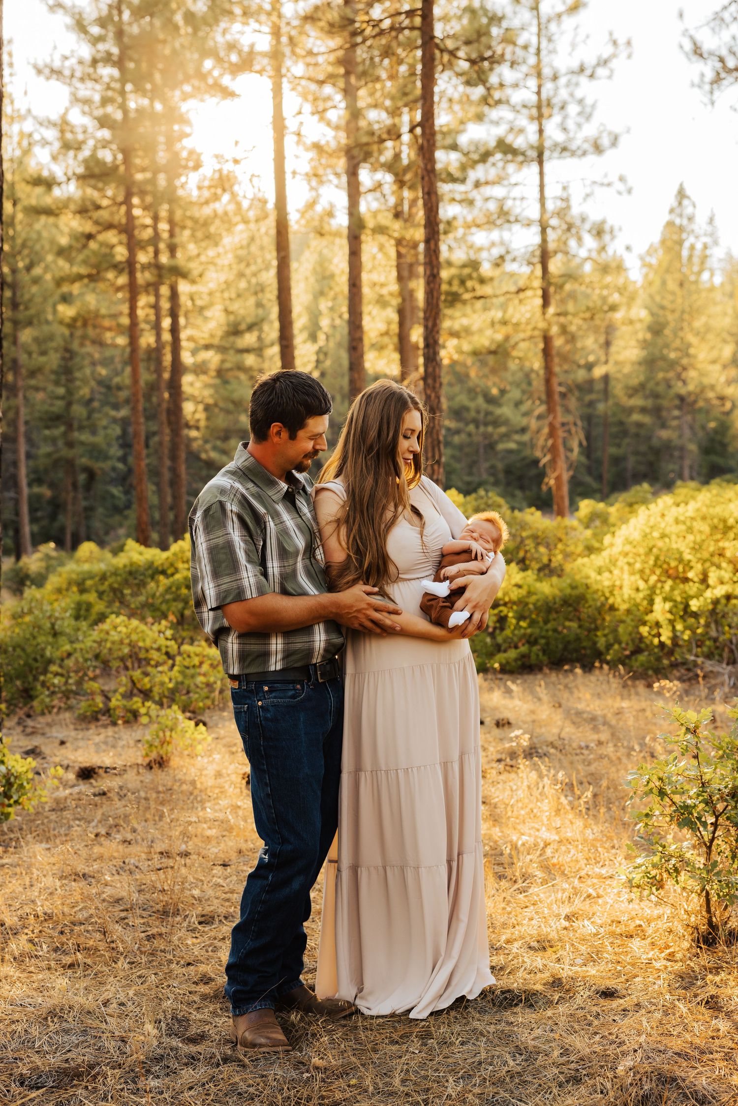 Family of three sharing an intimate moment in a pine forest during golden hour.