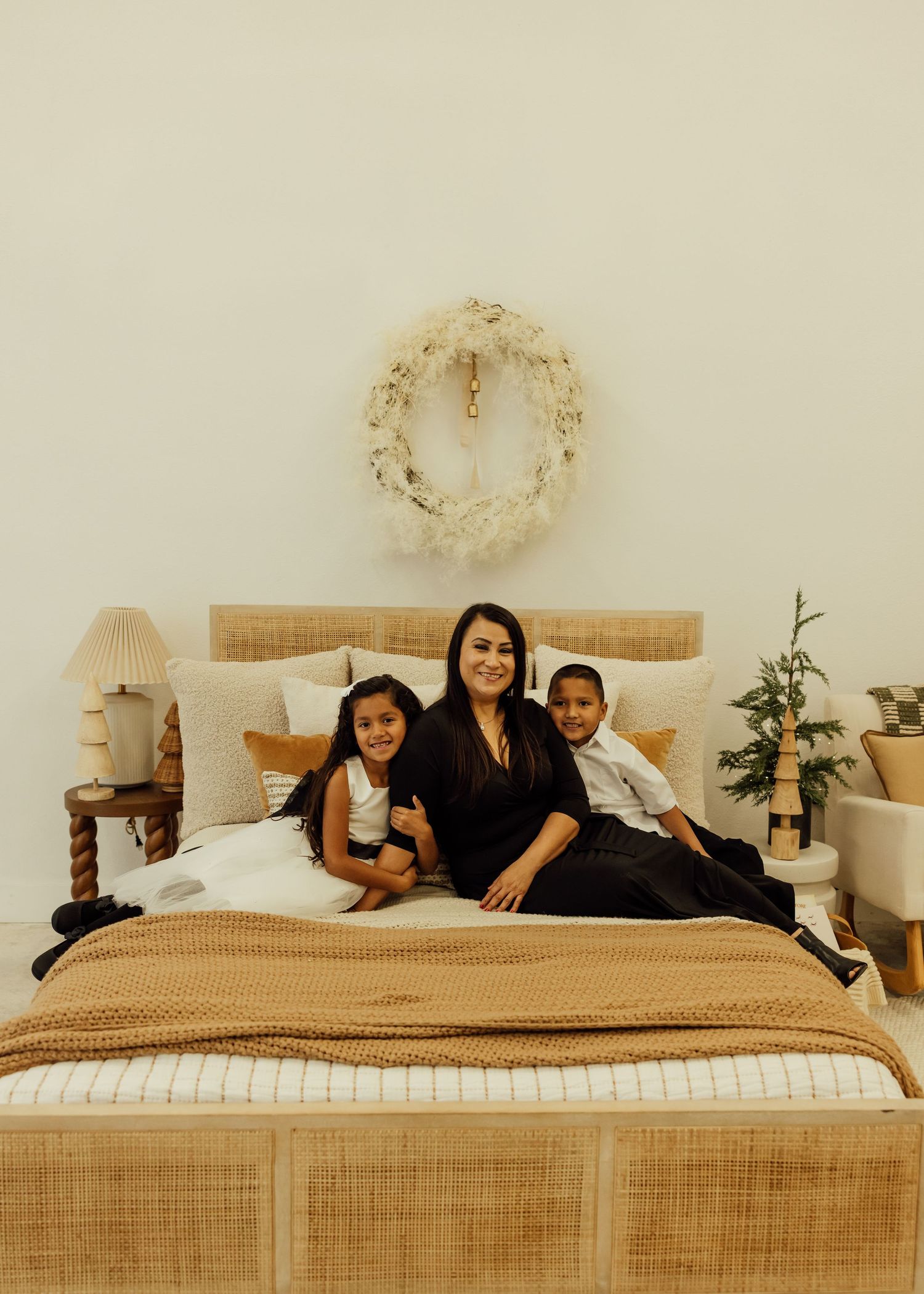 Family relaxing together on a beige bed with decorative wreaths on wall.