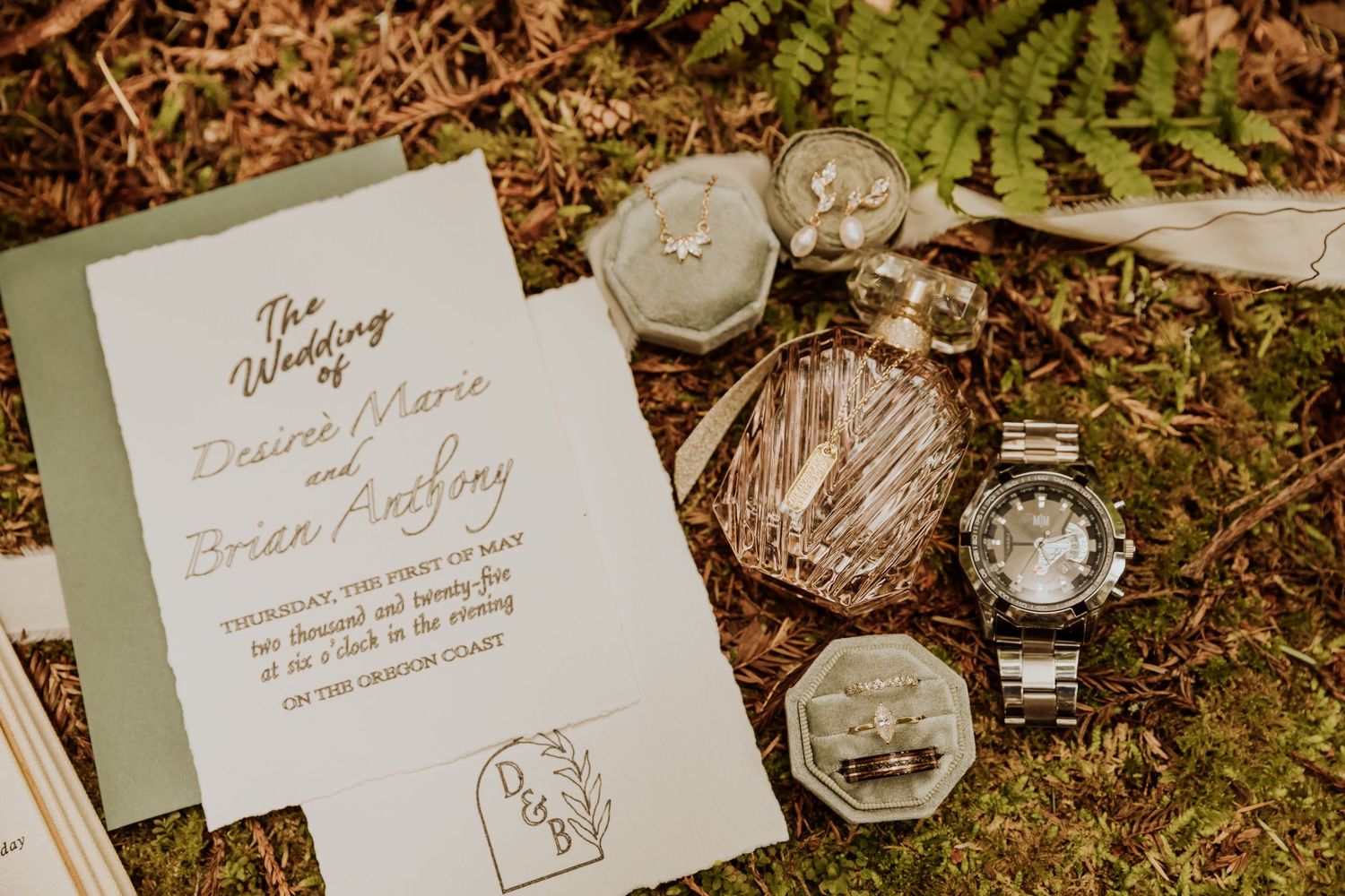 Wedding stationery and ring boxes arranged on mossy ground with natural greenery.