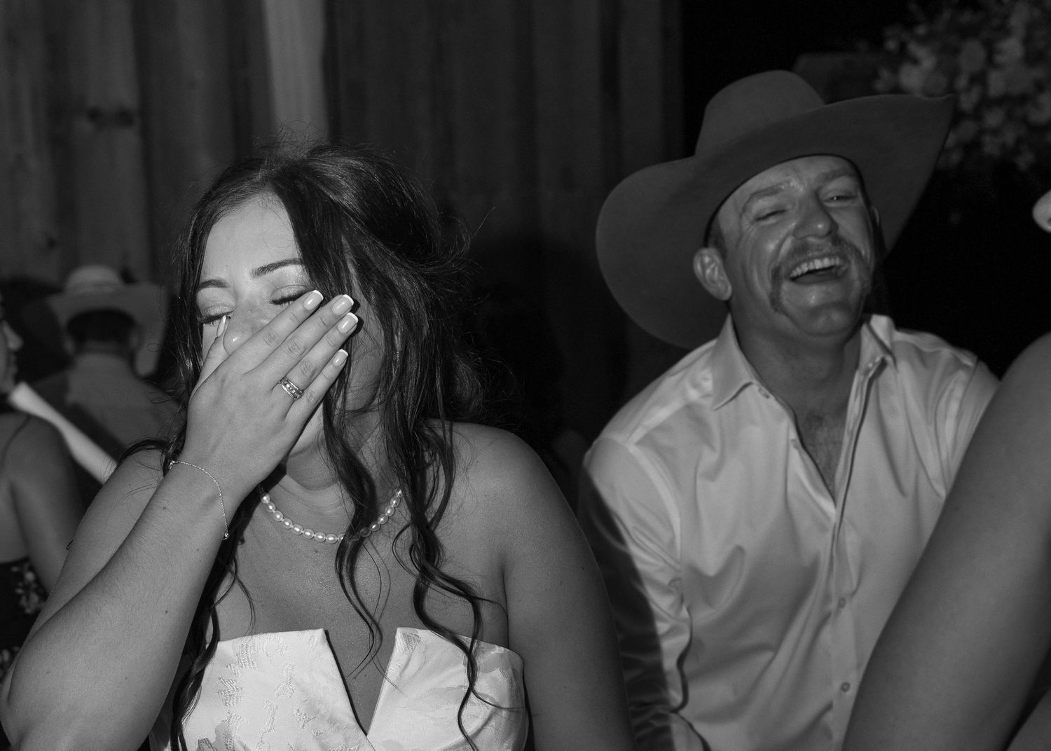 Candid black and white reception moment capturing joyful laughter between newlyweds.