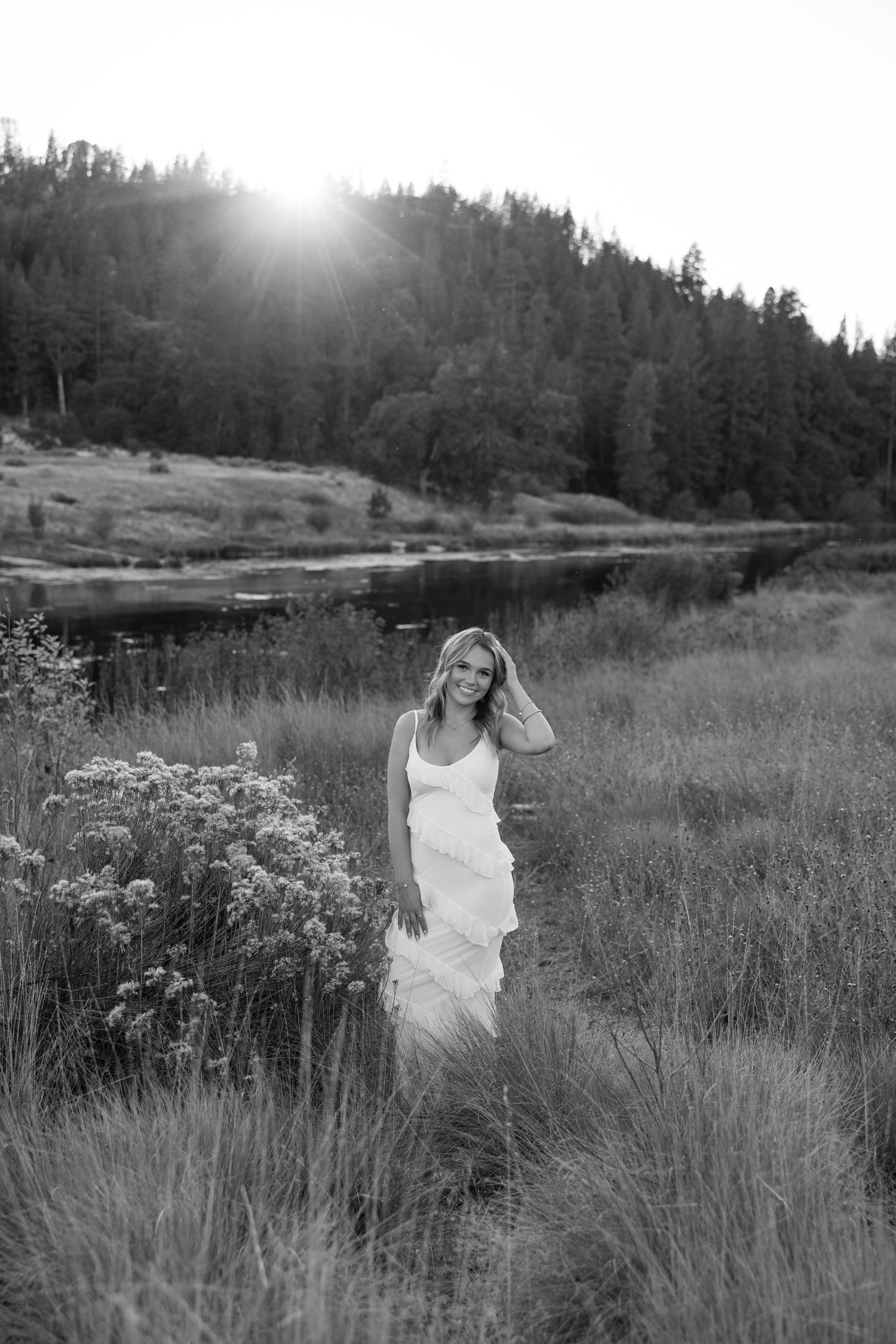 Ethereal black and white portrait in flowing white dress near mountain lake at sunset.