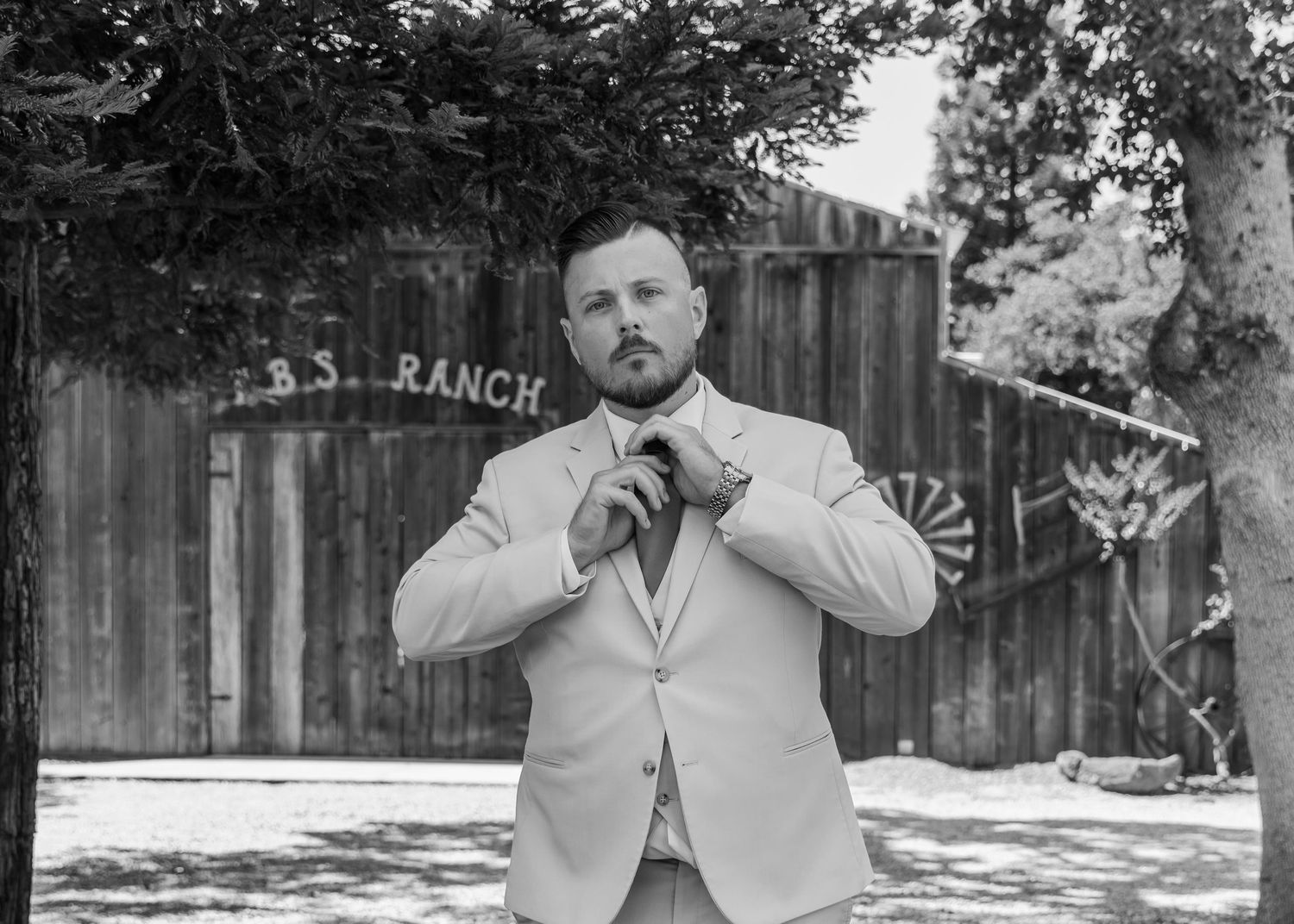 Groomsmen in light colored suits posing outdoors near wooden ranch buildings.