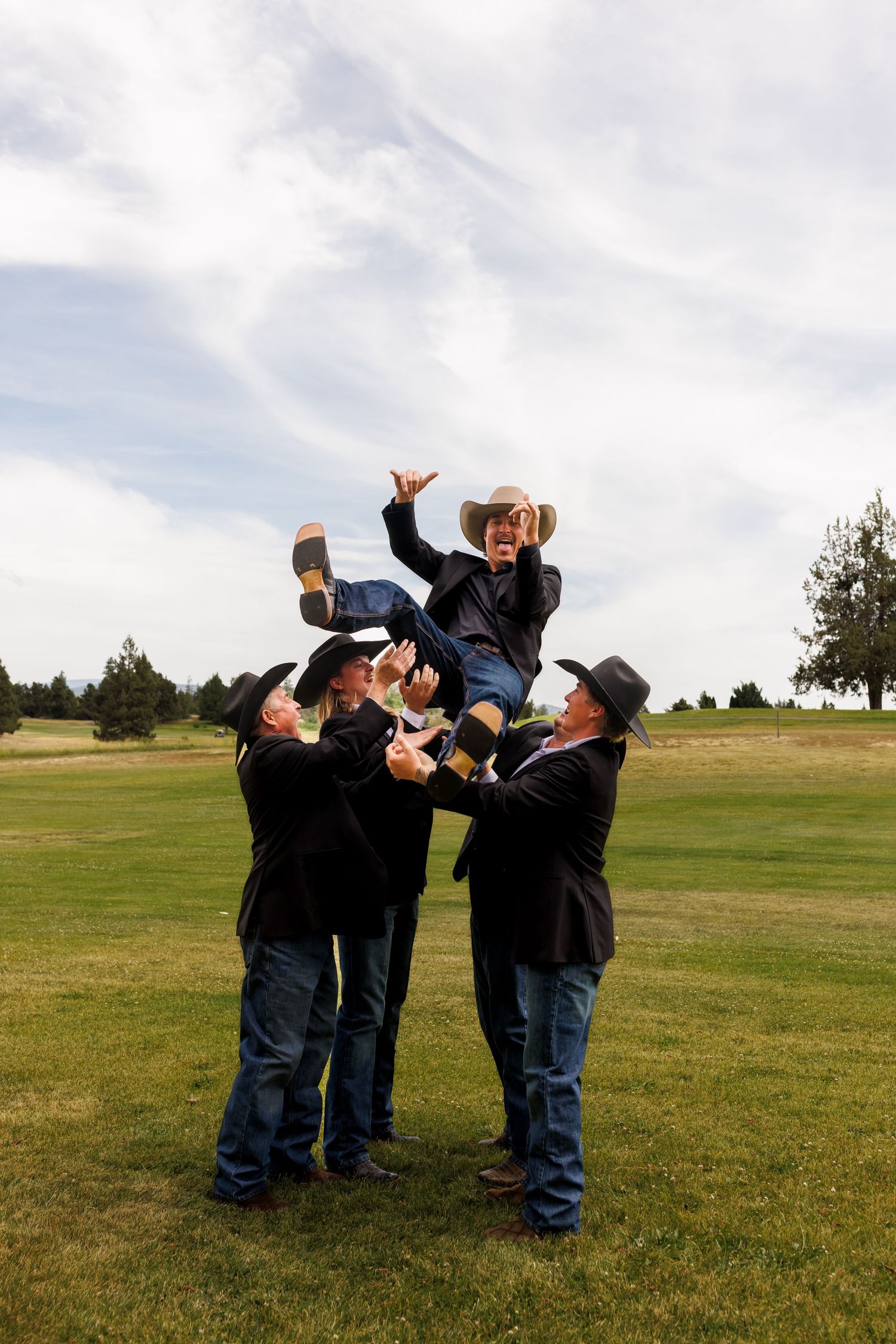 Groomsmen in navy suits playfully drinking from bottles while standing in a grassy field.
