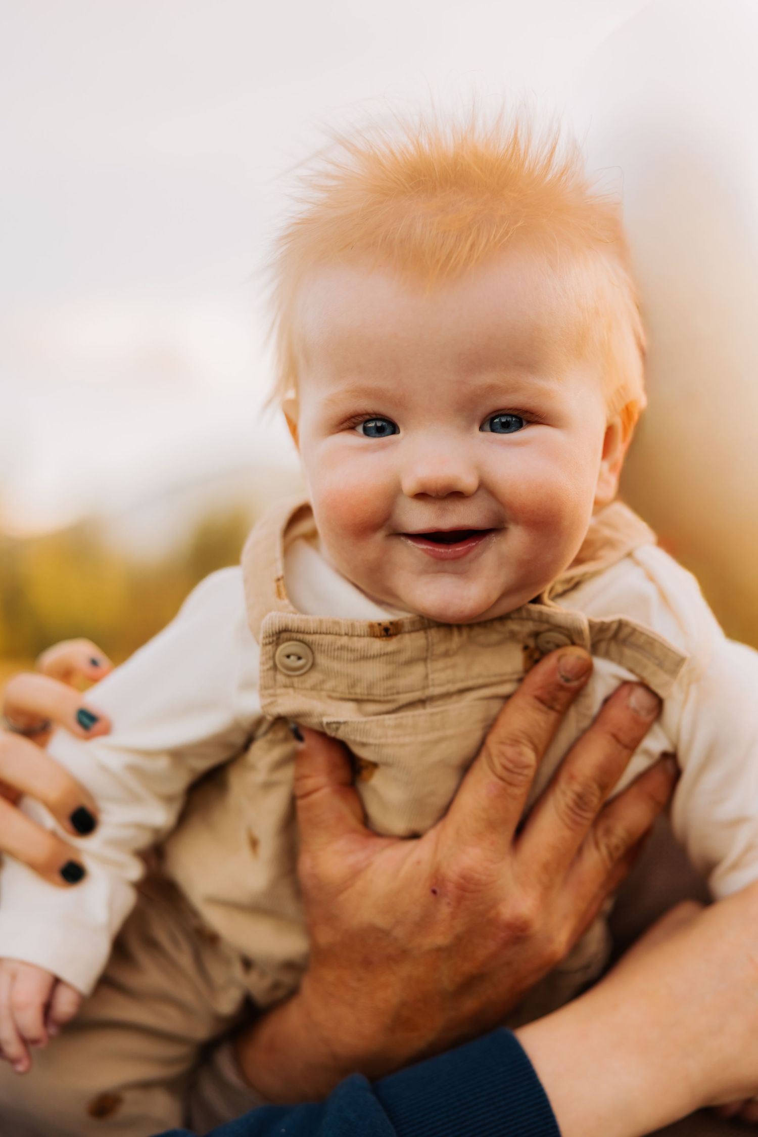 A close-up portrait of a smiling baby wearing tan overalls.