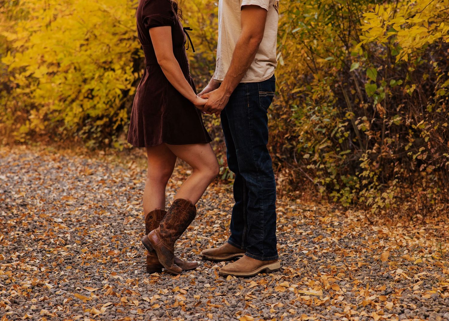 Couple's feet shown standing close together on autumn leaf-covered ground.