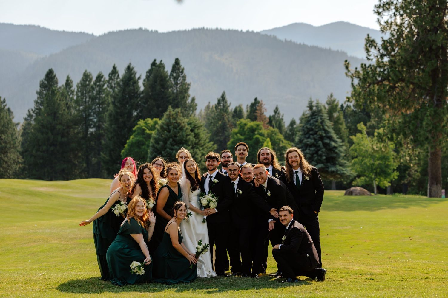 Wedding party poses on golf course with mountain and forest backdrop on a beautiful day.
