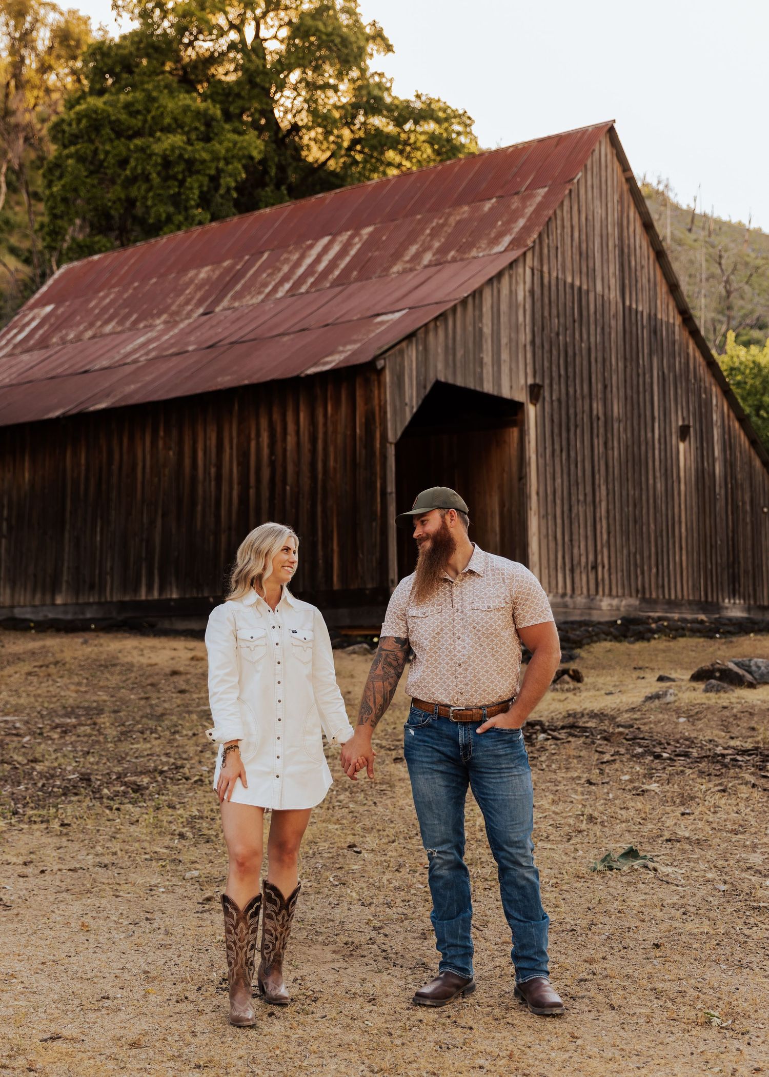 Couple holding hands while walking in front of an old wooden barn during sunset.