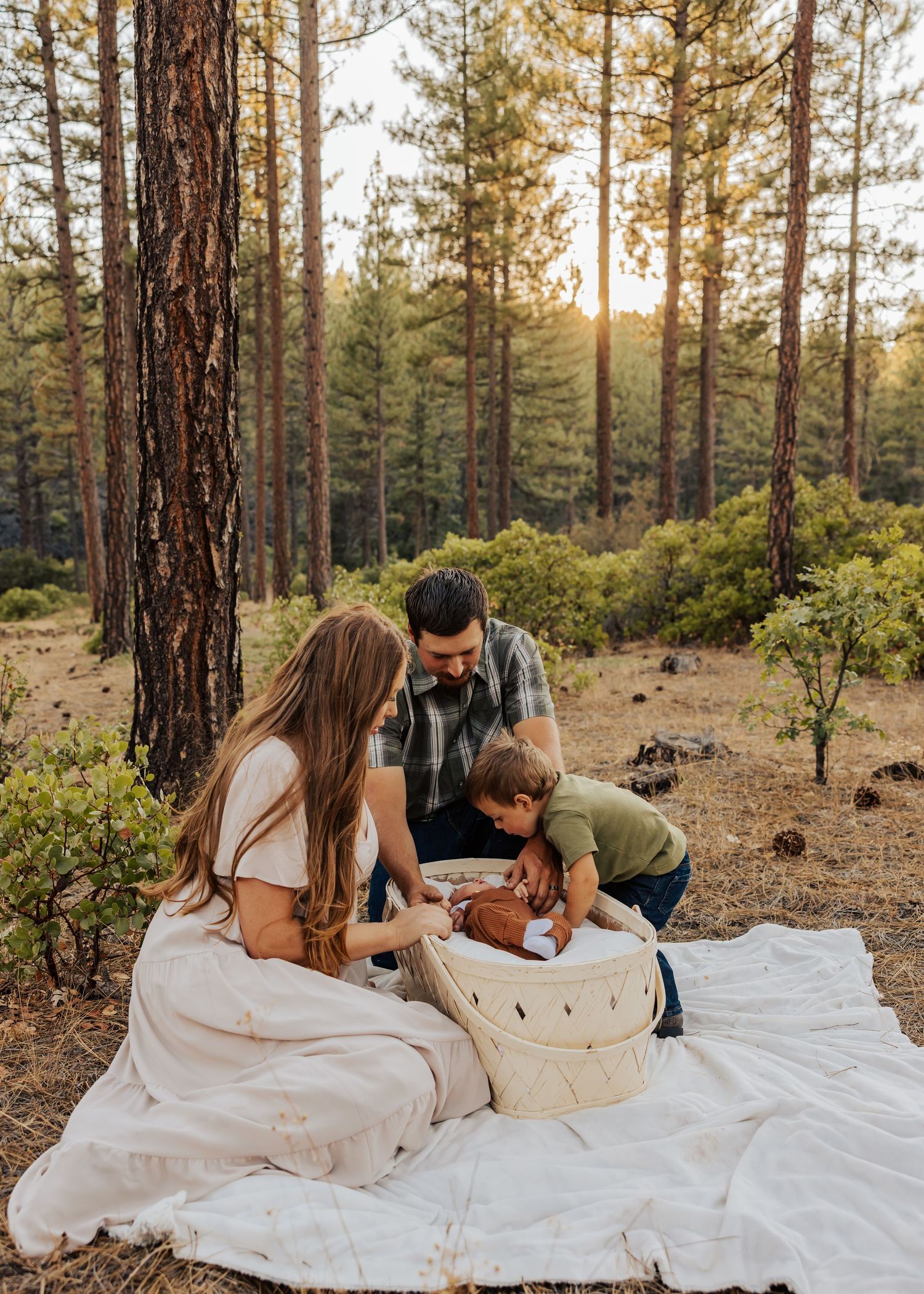 Family lying on white blanket having tender moments together in sunny pine forest setting.
