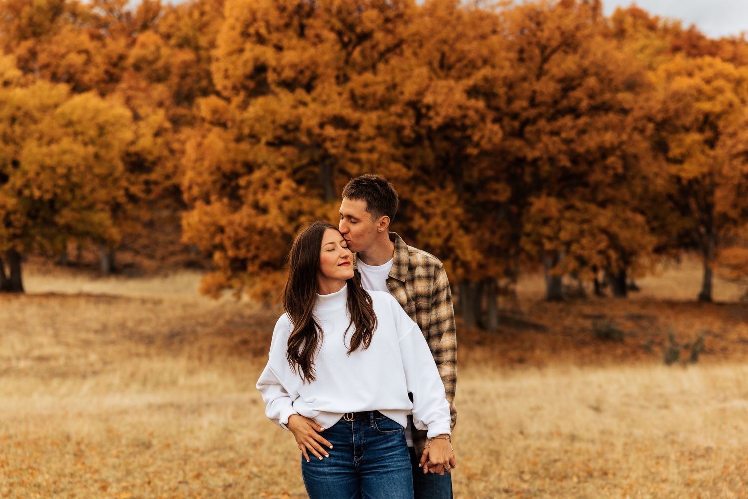 Couple embraces in a romantic autumn photoshoot with golden foliage in the background.