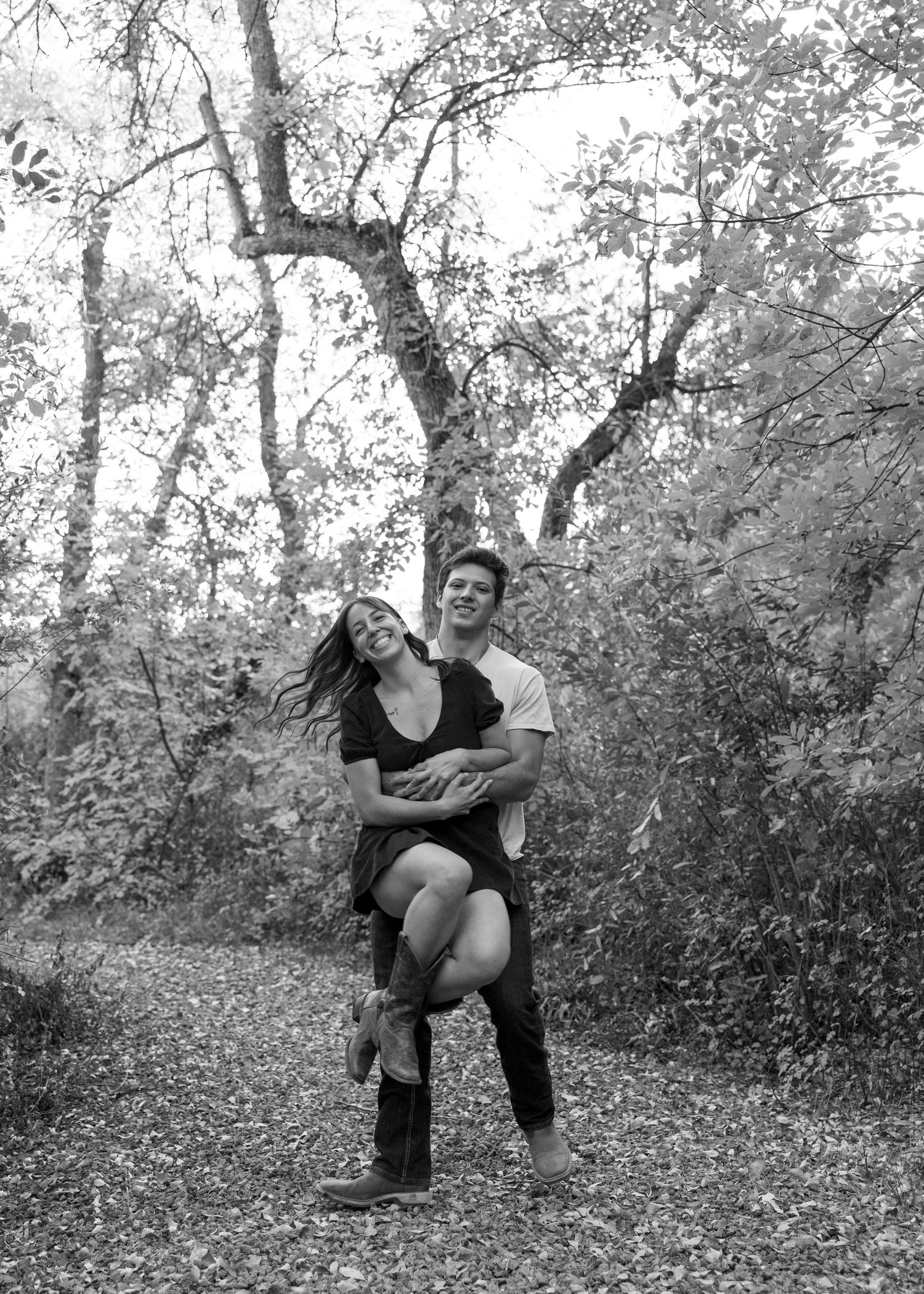 Black and white photo series of a couple playfully posing together in a wooded outdoor setting.