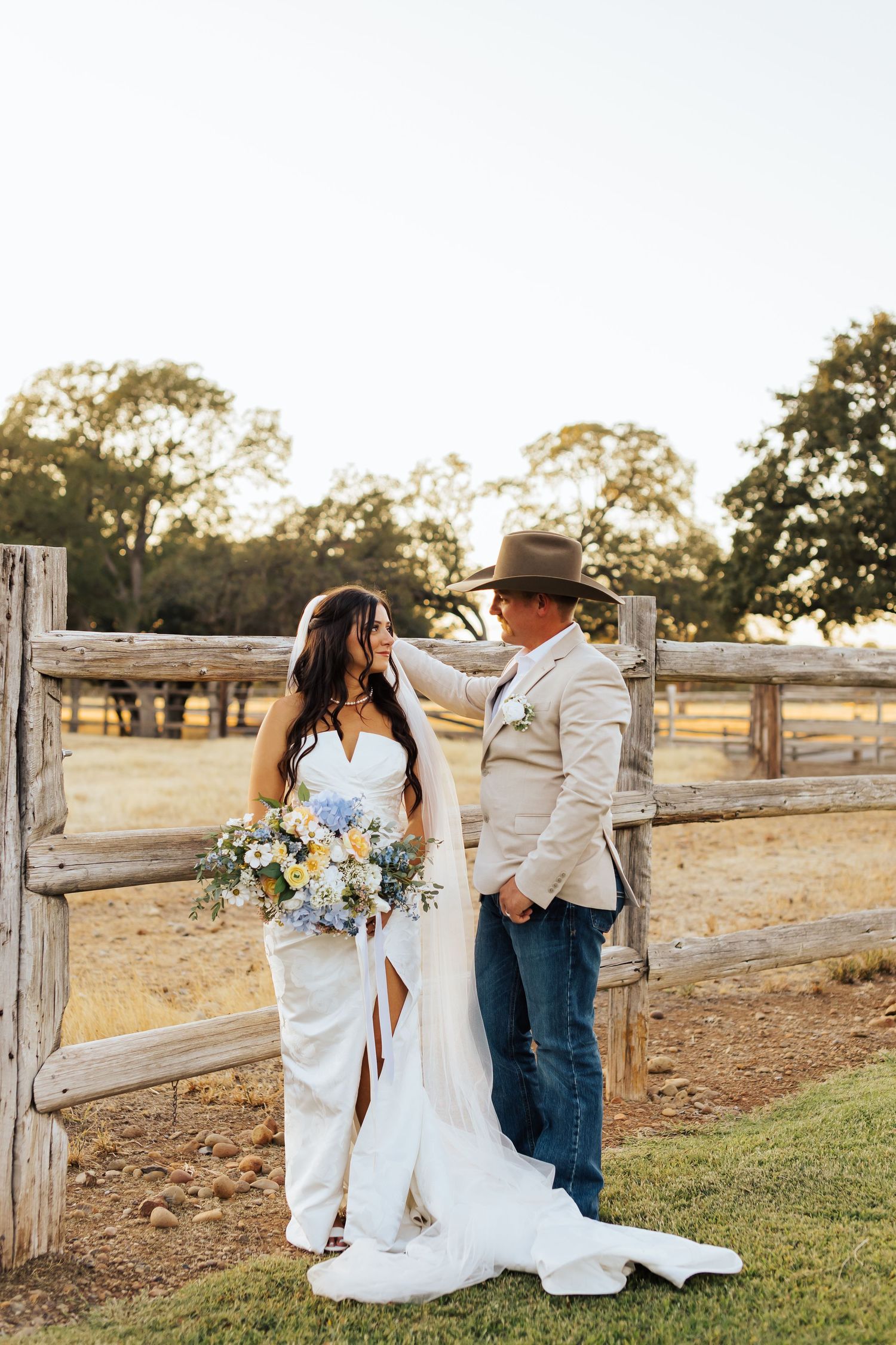 Country wedding photo session by a rustic wooden fence at sunset.