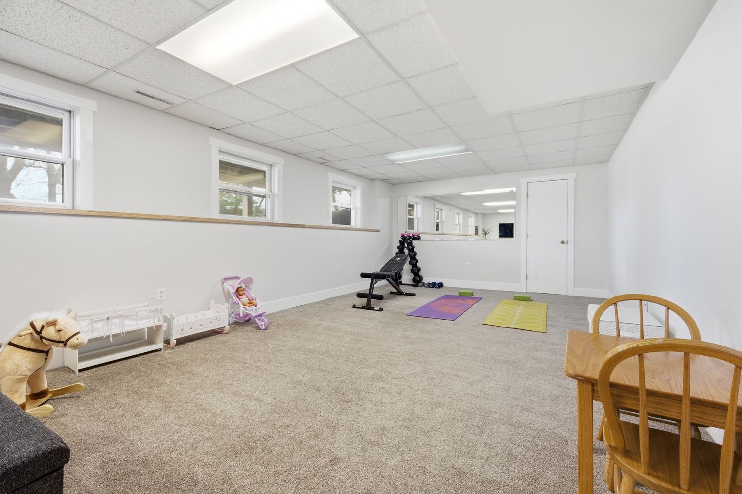 Finished basement with carpet, drop ceiling, gym equipment, mirrors, and natural light from small windows.