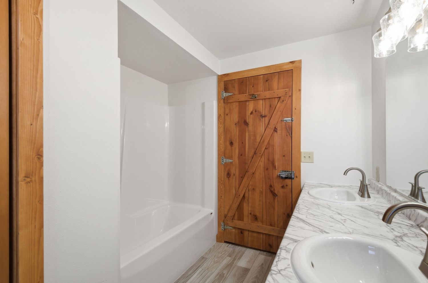 Bright white bathroom interior with wooden door and chrome fixtures showcasing modern farmhouse design elements.