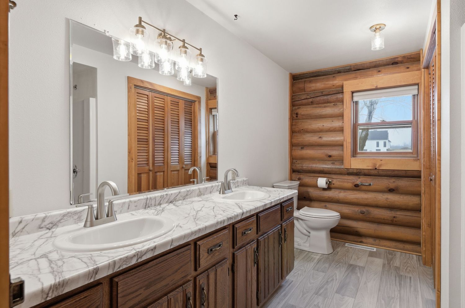 Modern bathroom with log cabin walls features marble countertops, vessel sink, and contemporary track lighting.