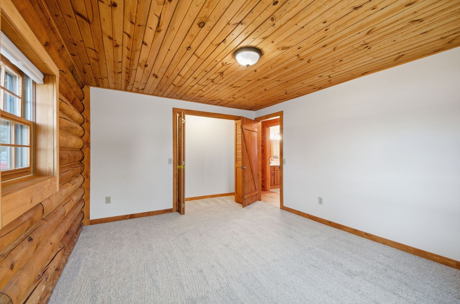 A rustic room interior with wooden plank ceiling, white walls, and large windows letting in natural light.