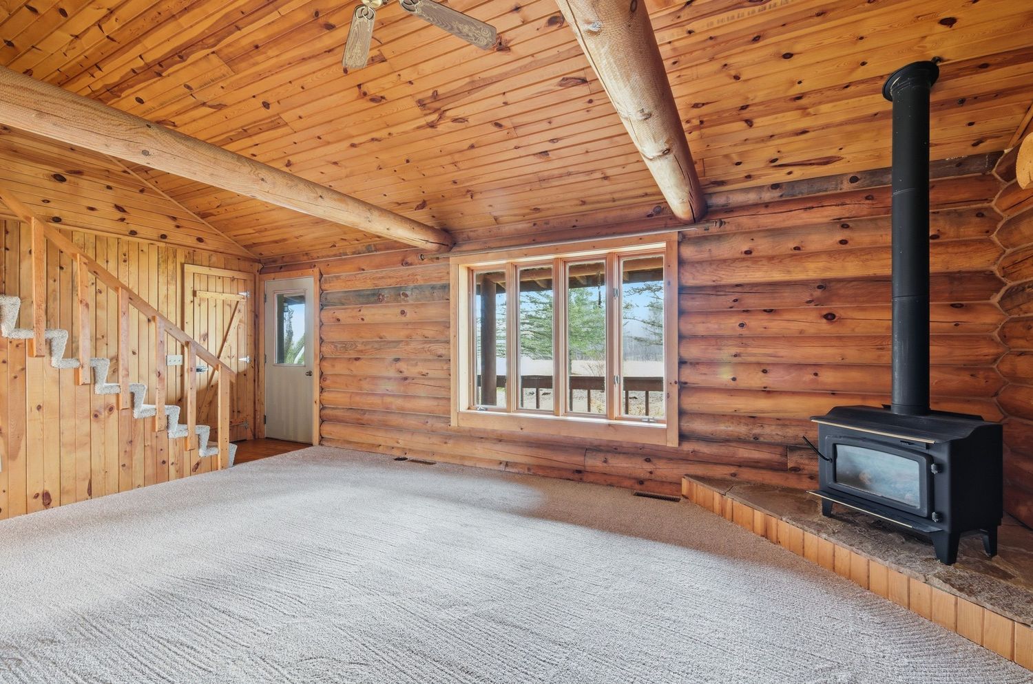 Interior of a rustic log cabin with wooden walls, vaulted ceilings, and large windows letting in natural light.