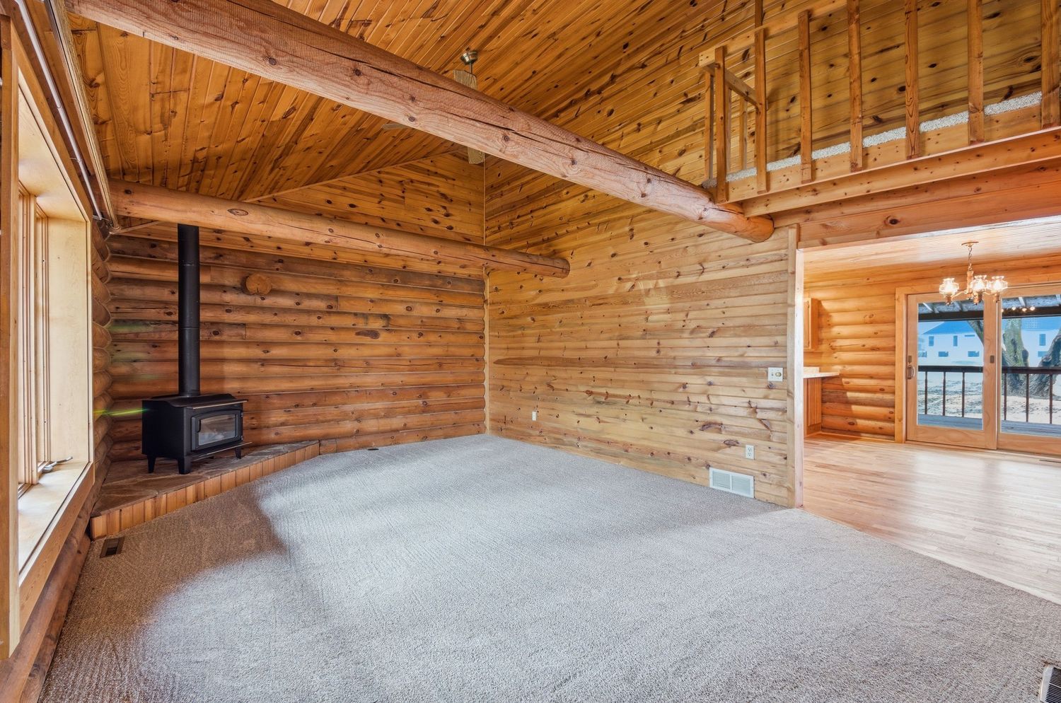 Interior panorama of rustic wooden cabin with exposed beams, hardwood floors and large windows letting in natural light.