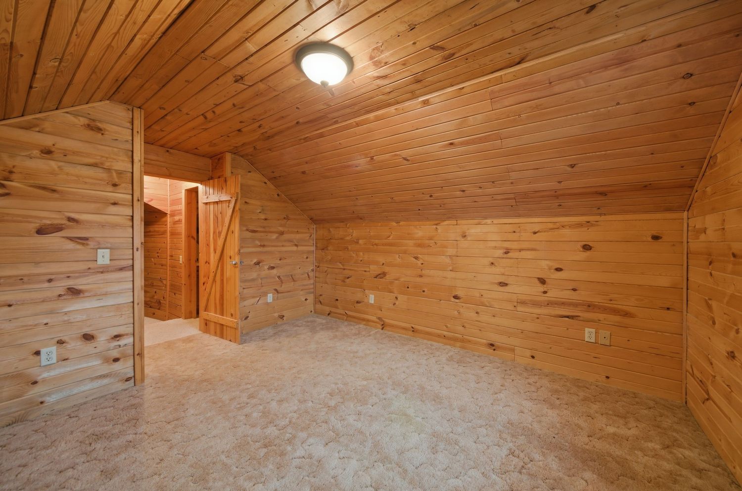 Rustic wood-paneled interior room with exposed ceiling beams and warm lighting creates a cozy cabin atmosphere.
