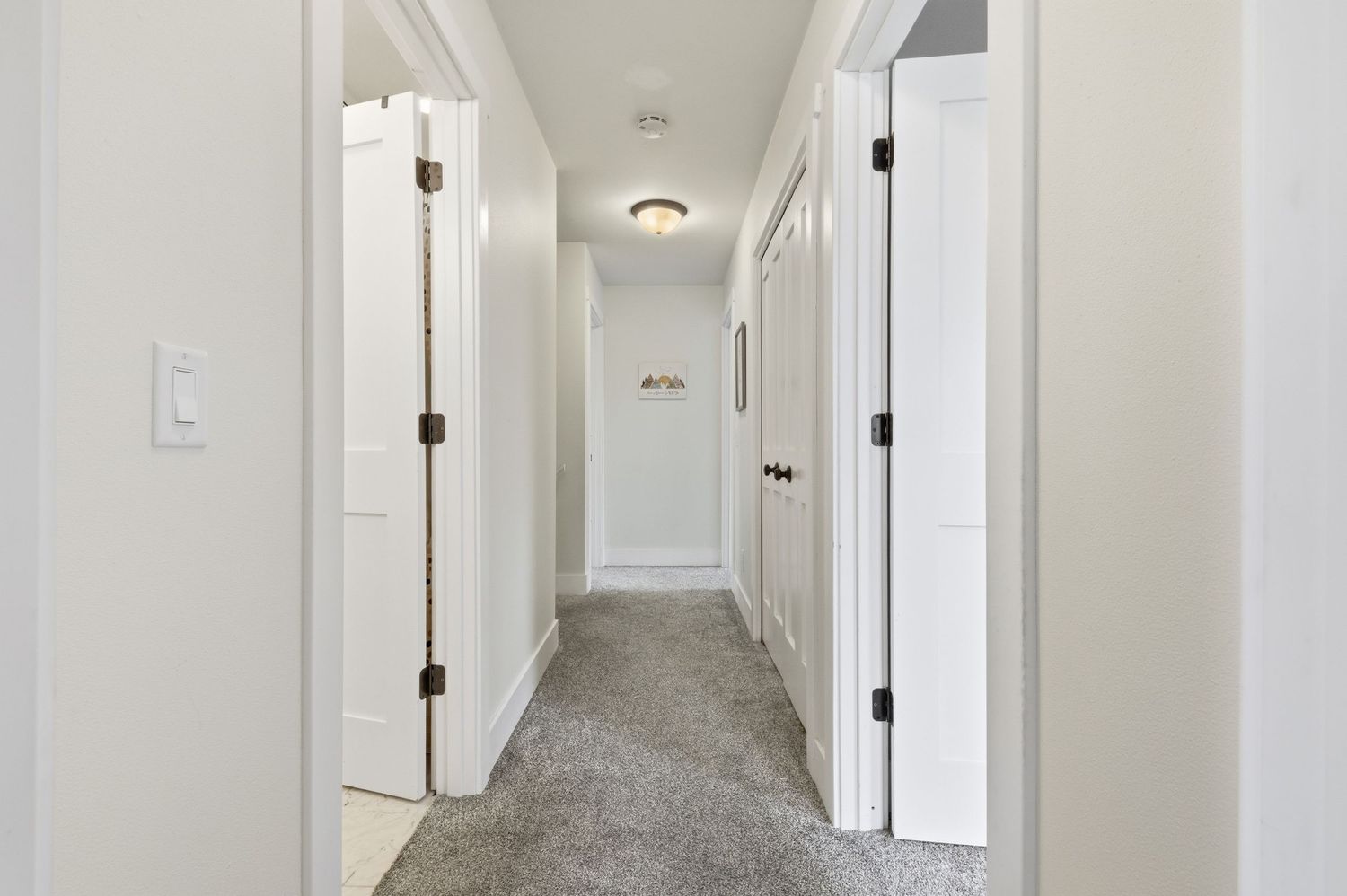 Bright carpeted hallway with white doors, black hinges, and neutral walls leading to a well-lit entryway.