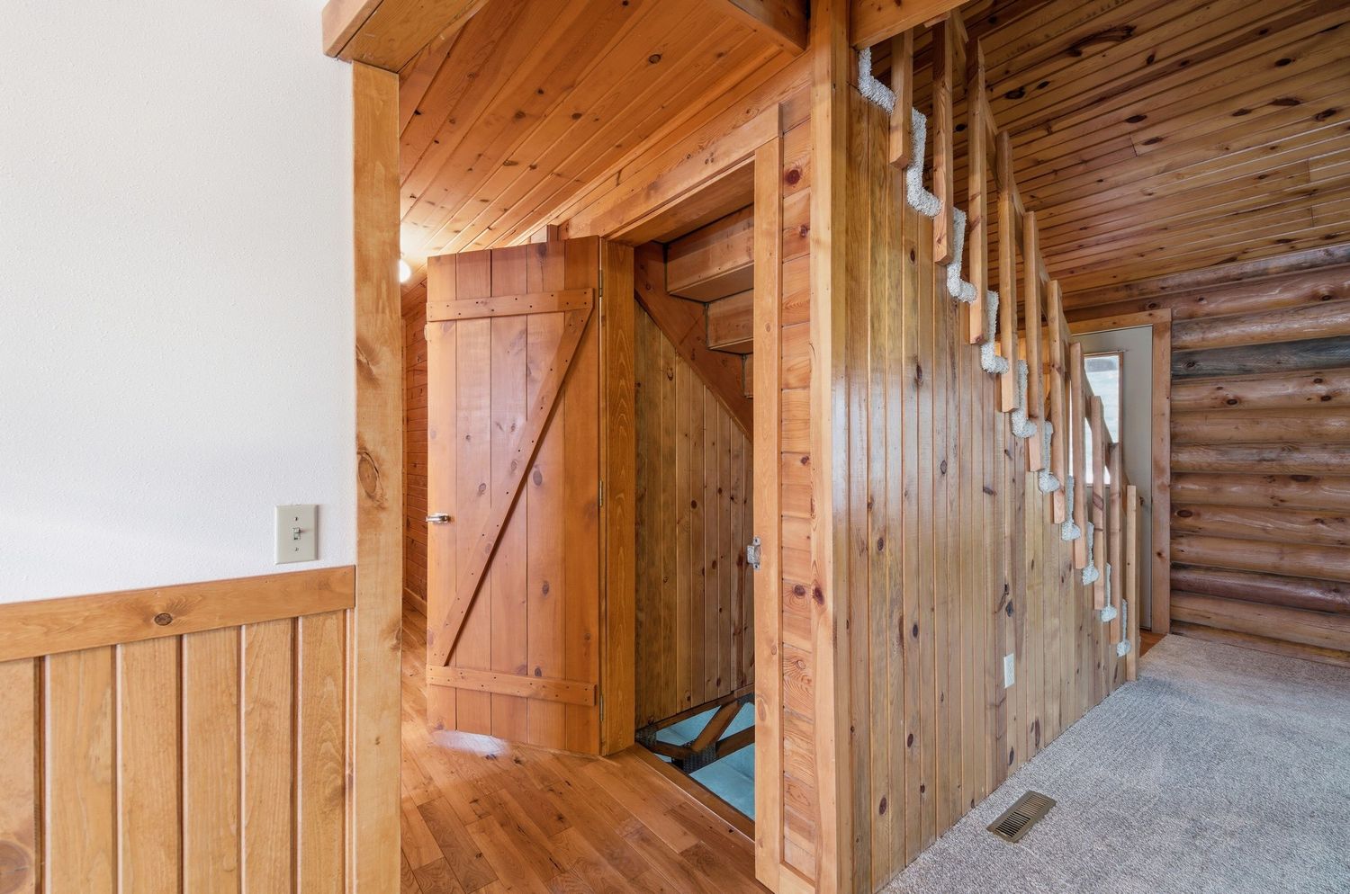 Rustic wooden barn interior with exposed beams and natural lighting showing a long hallway with stalls.