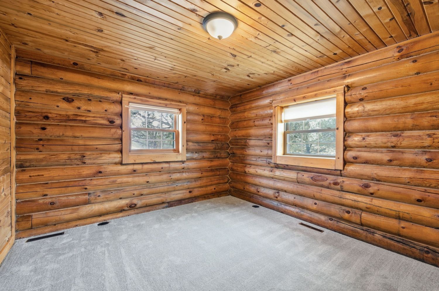 Rustic log cabin interior with warm wood paneled walls, ceiling beams, and small windows letting in natural light.