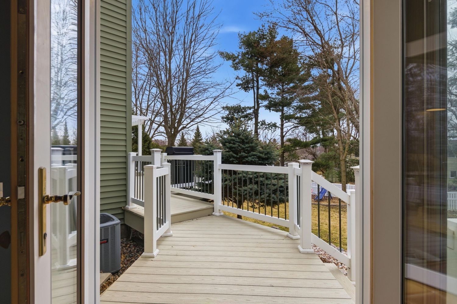 Wooden deck with white railings overlooking a landscaped backyard with mature trees on a clear day.