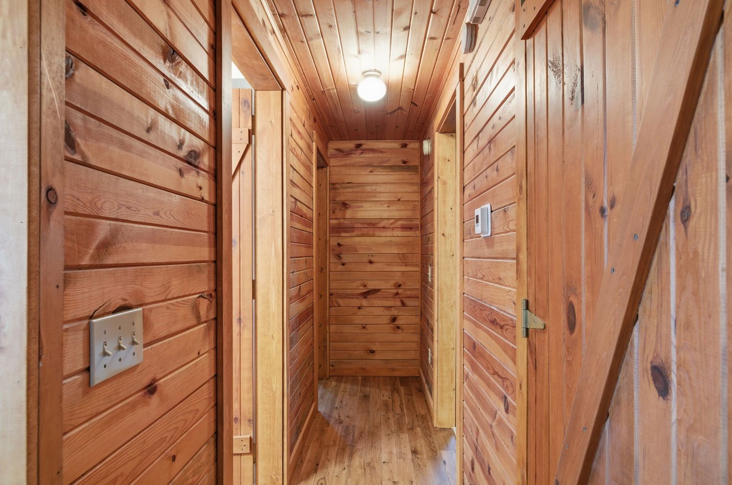 Rustic wooden hallway with diagonal paneling and exposed beams features warm lighting and natural wood tones throughout.