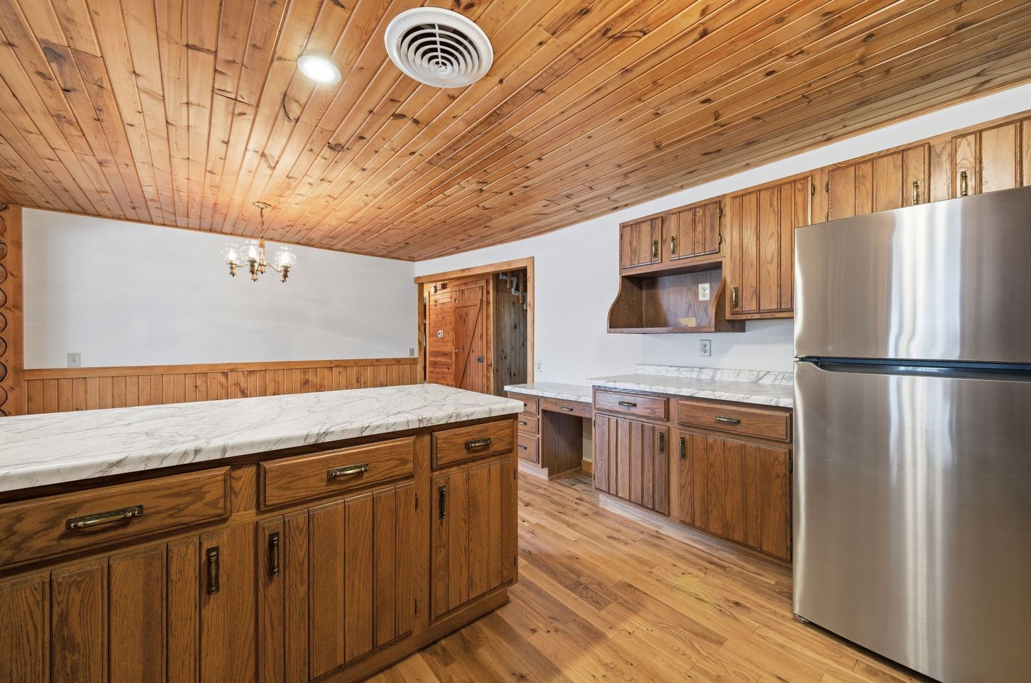 Modern kitchen with wood paneled ceiling and walls features stainless steel appliances and white countertops.