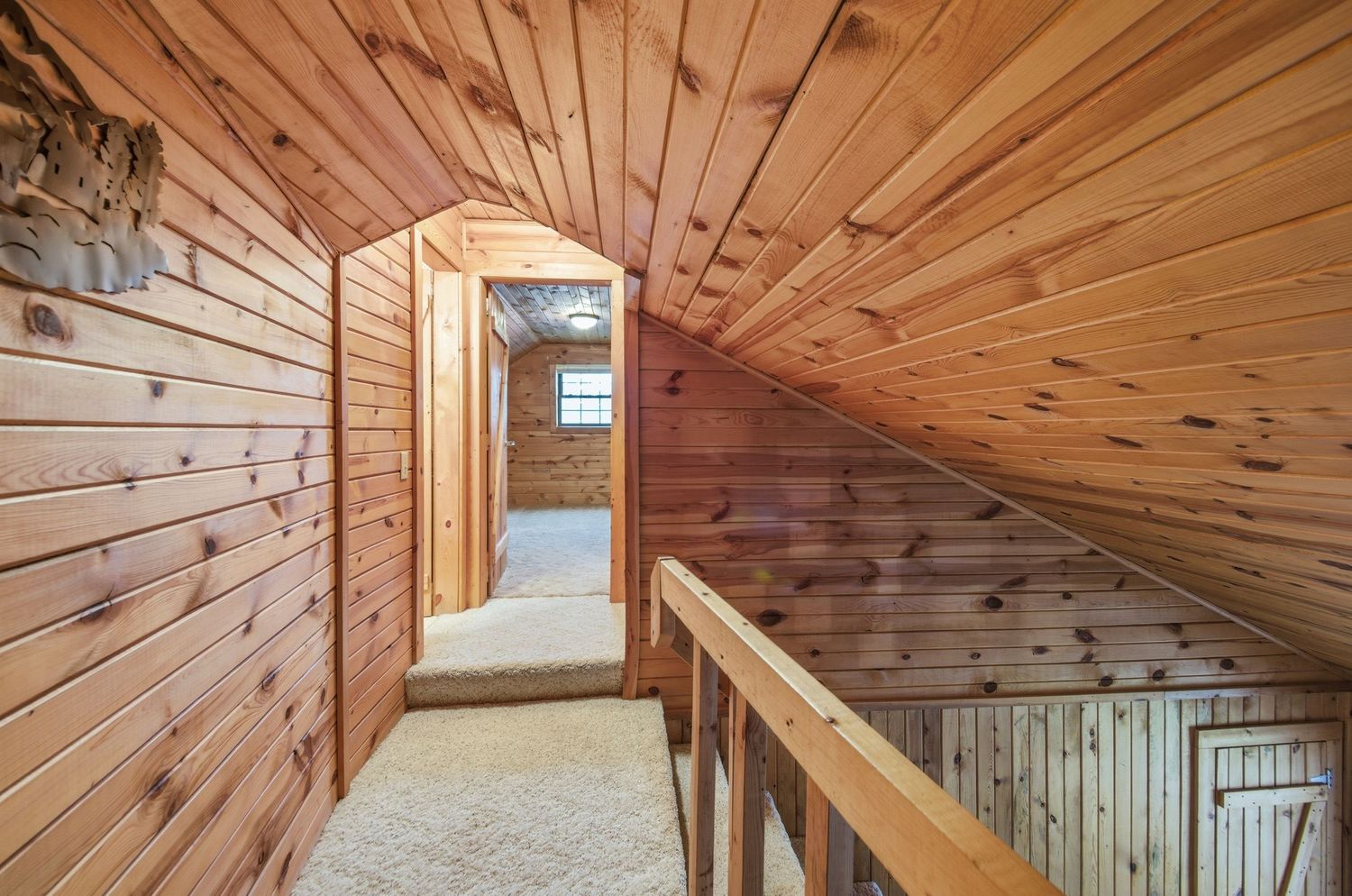 Interior view of a wooden cabin hallway with natural pine paneling and a railing along the upper level.