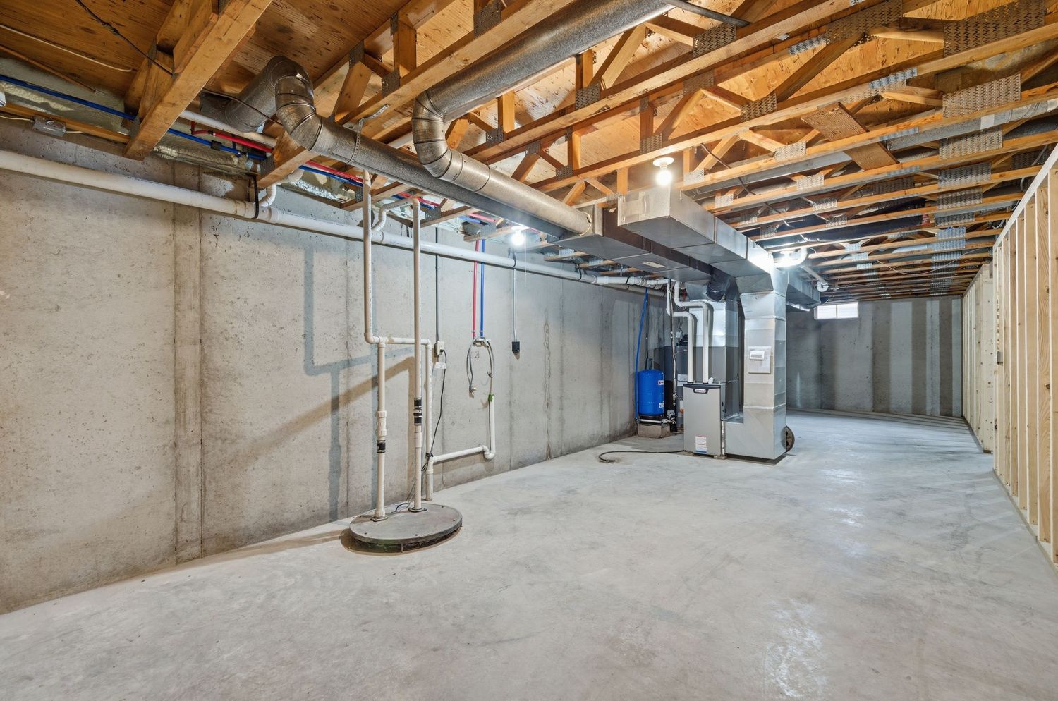 Unfinished basement interior showing exposed wooden beams, concrete floors, and utility installations in progress.