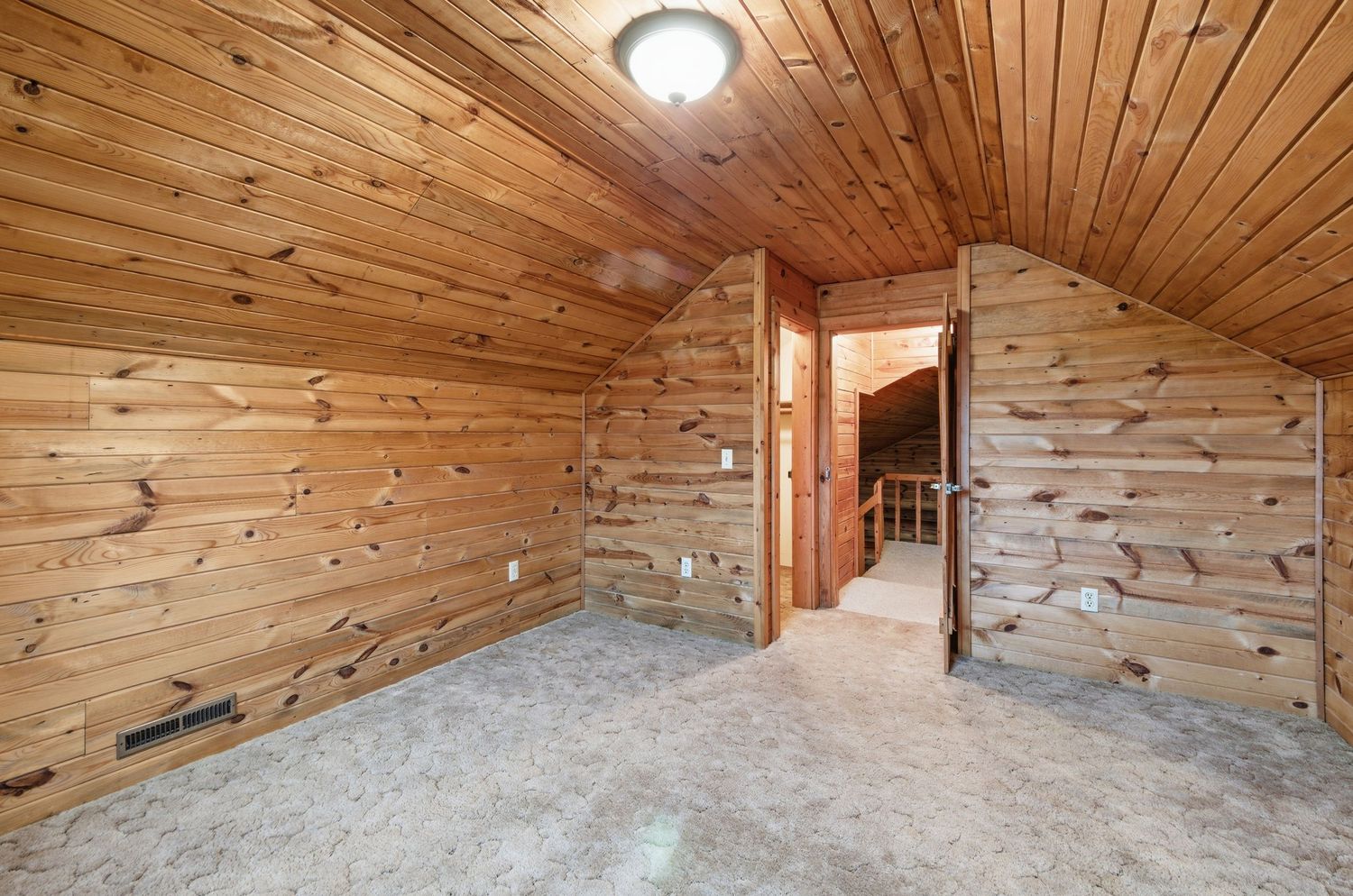 Unfinished attic space with wood plank ceiling and exposed floor joists in rustic cabin interior.