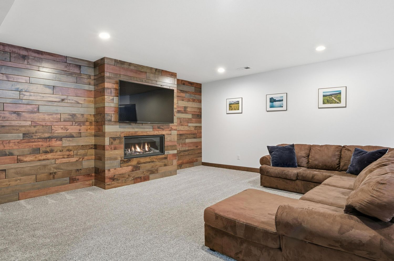 Modern basement living room with brown sectional sofa, exposed brick accent wall, and recessed lighting.