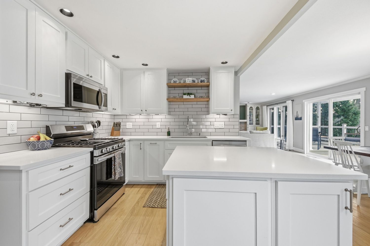 Modern white kitchen with subway tile backsplash, stainless steel appliances, quartz island, and hardwood floors.