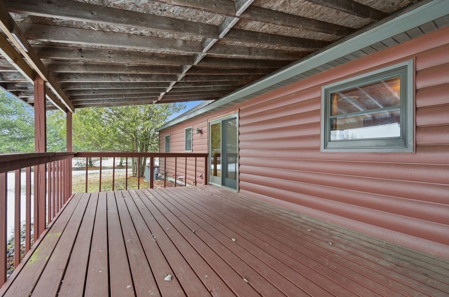 Long covered wooden deck with pink siding and exposed beams stretches along the side of a building.