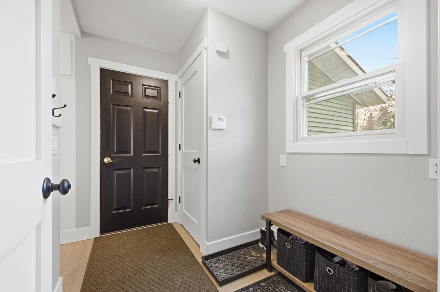 Bright mudroom entryway with dark front door, white trim, bench with storage baskets, and natural light from window.