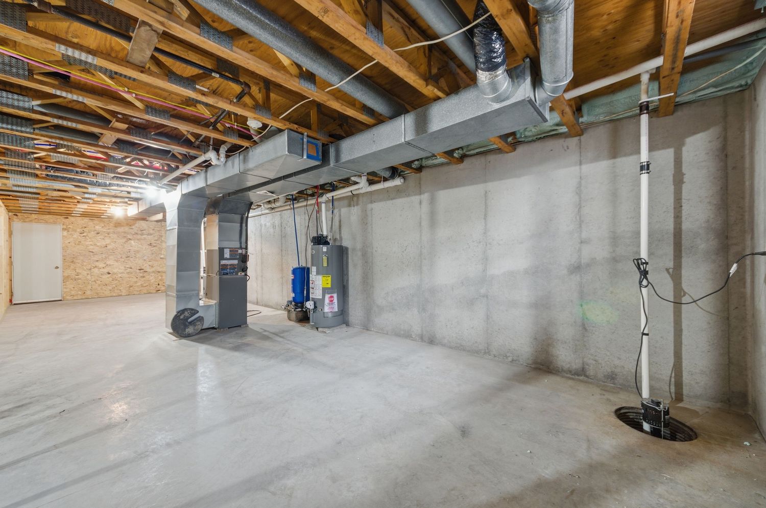 Unfinished basement interior showing exposed wooden ceiling joists, concrete walls, and utility systems.