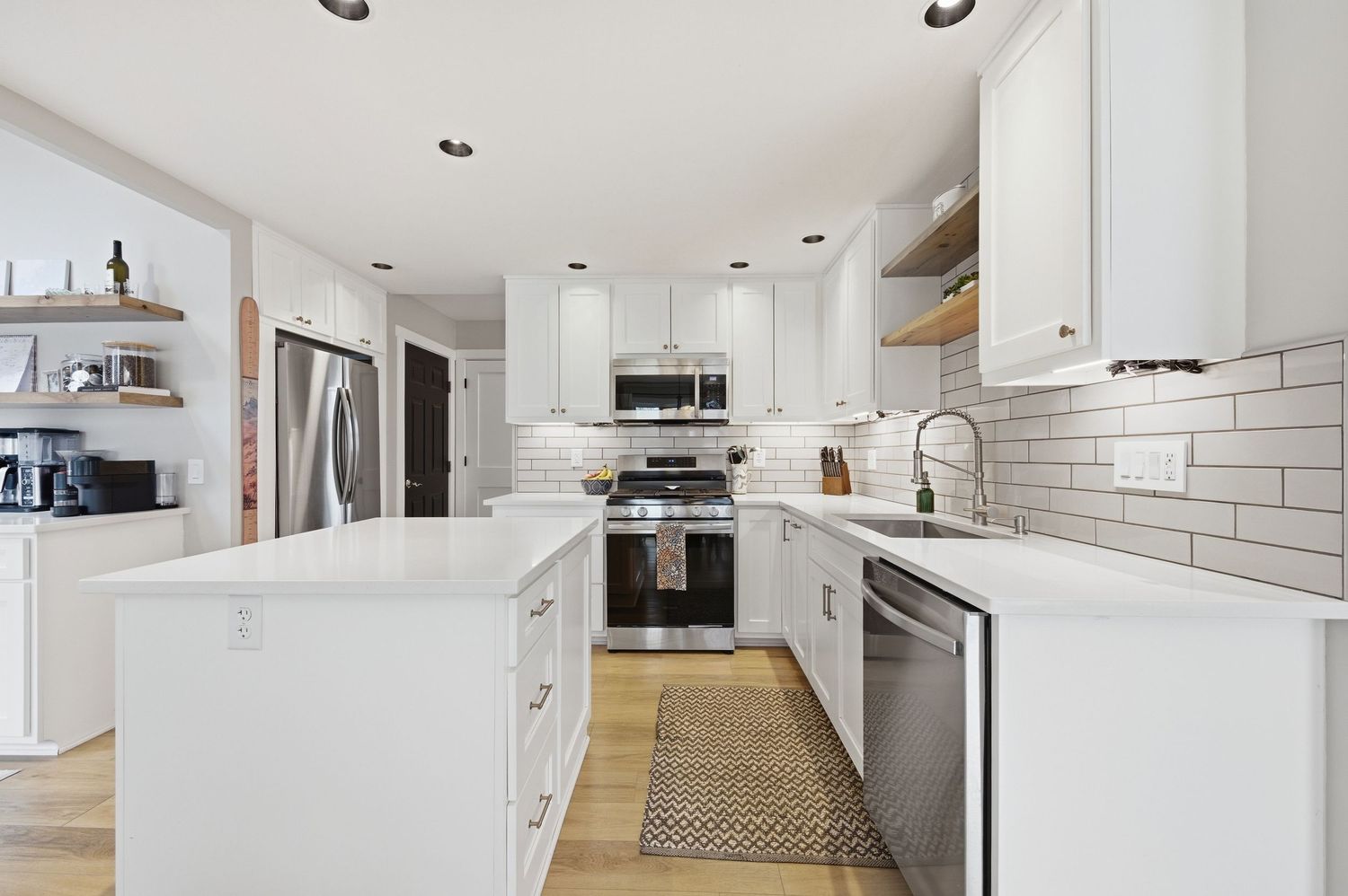 Modern white kitchen with stainless steel appliances, subway tile backsplash, center island, and hardwood floors.