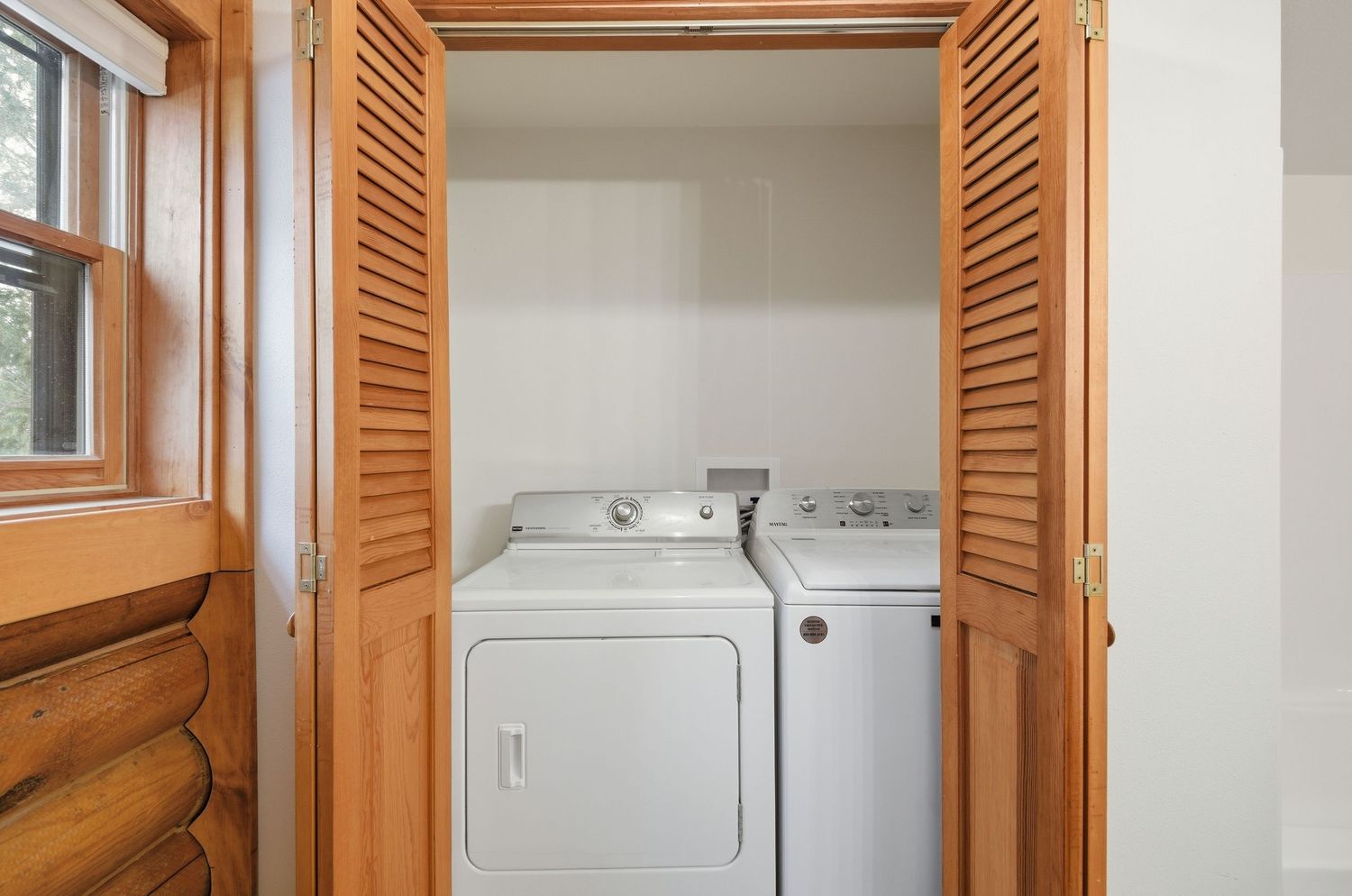 Wooden louvered doors open to reveal a white stackable washer and dryer unit in a laundry closet.