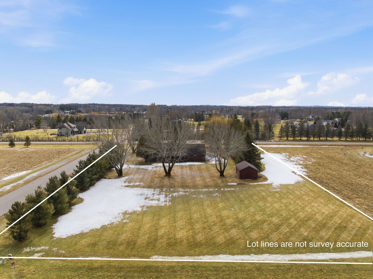 Aerial view of a rural property with snowy patches on yellow grass fields and tree lines under blue winter sky.